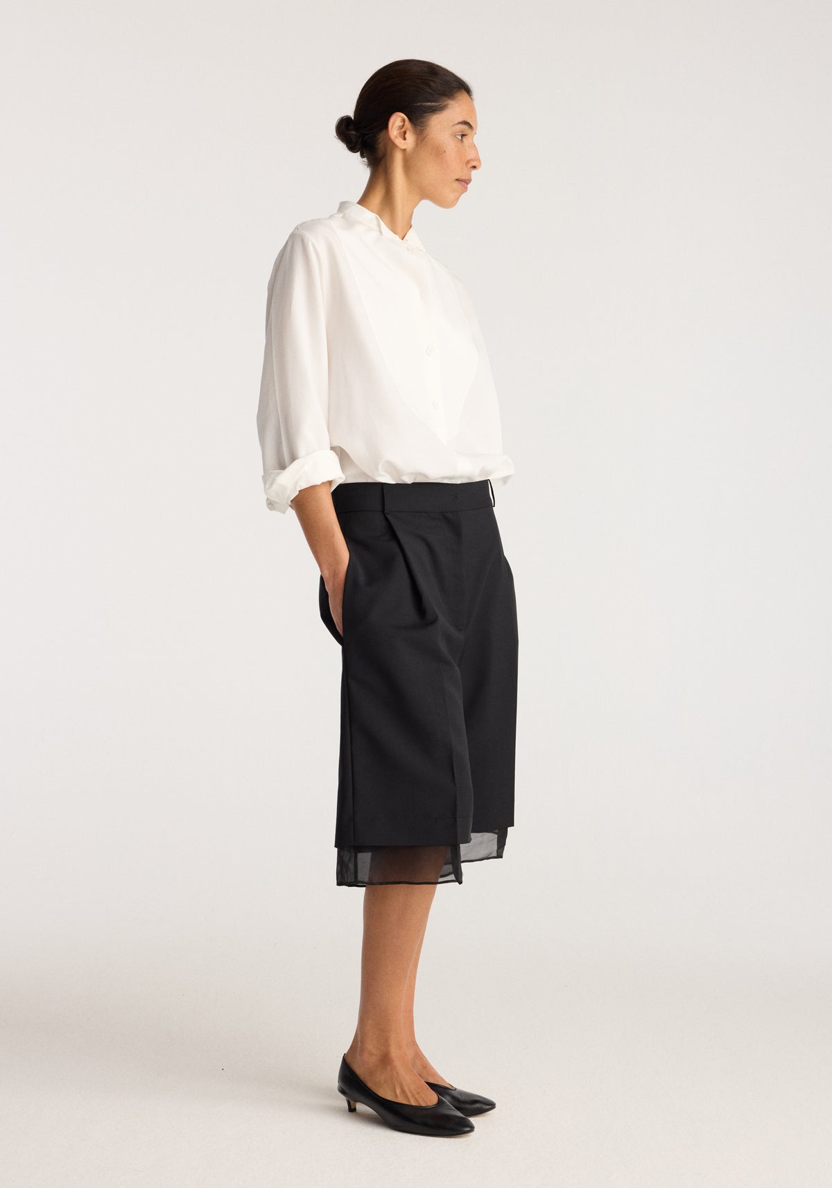 Organza lined shorts | black worn by a model with a white blouse and black flats, showing the knee length silhouette and sheer organza lining in profile