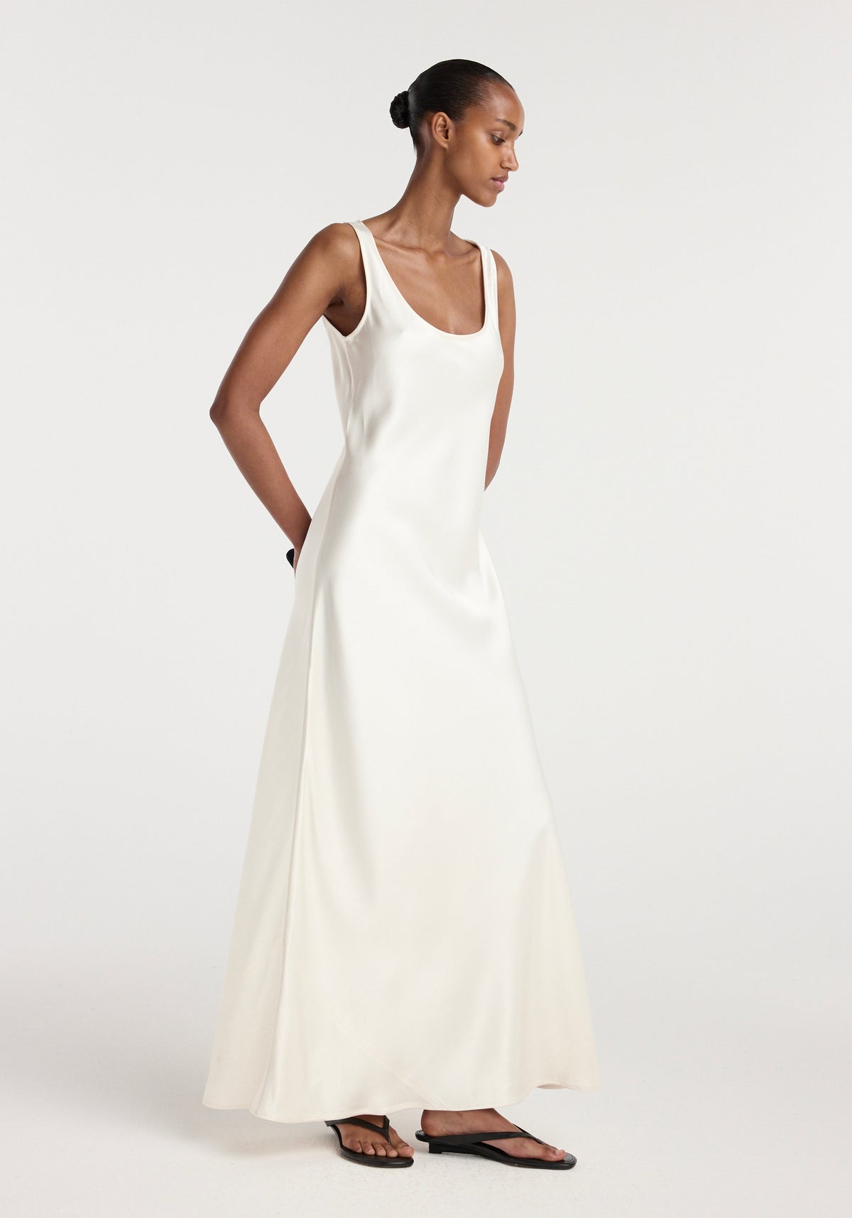 Woman wearing an elegant scoop neck satin dress in ivory with a flowing silhouette, styled with simple black flat sandals against a plain white background, Scoop neck satin dress | ivory.