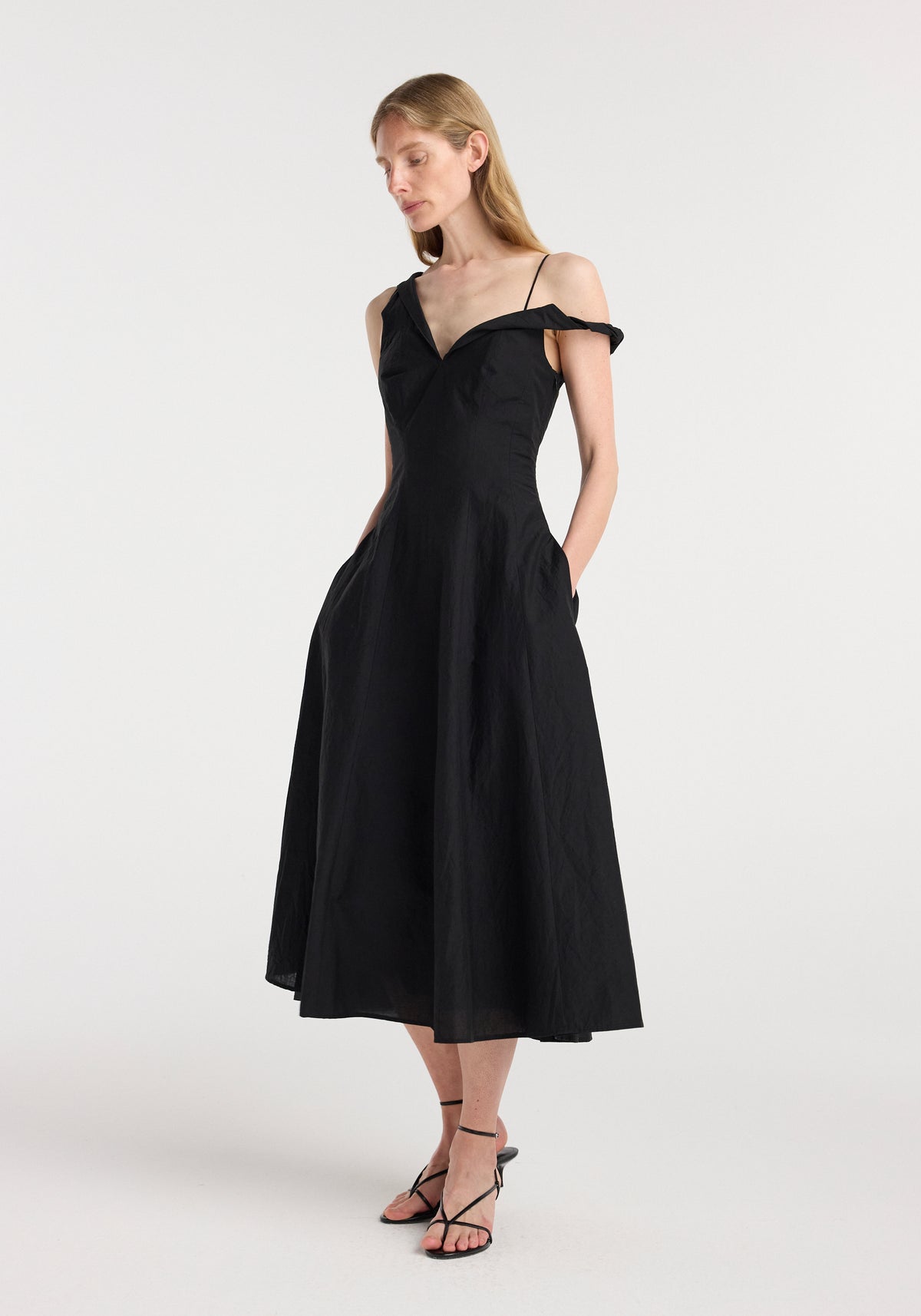 Woman wearing a sleeveless black dress with an off-shoulder twisted detail and midi length, styled with thin straps and a fitted waist, called Twisted shoulder dress | black.