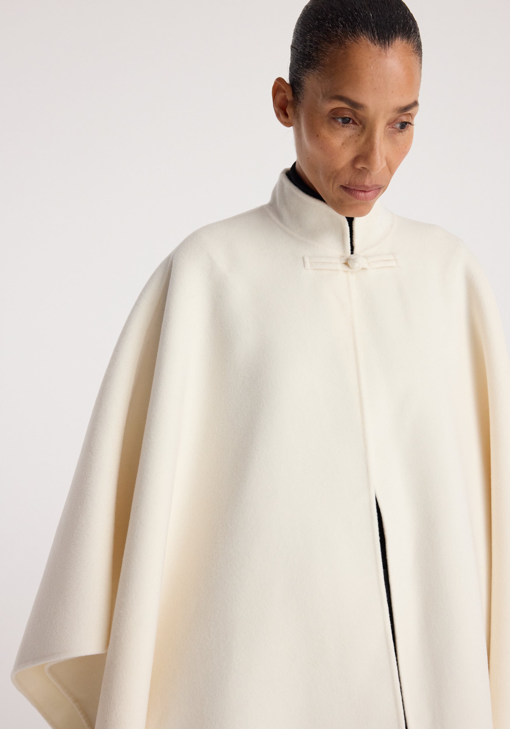 Woman wearing an off-white, high-neck double-faced pankou poncho with a clean, minimalist design and a subtle fastening at the collar, styled over a black top.