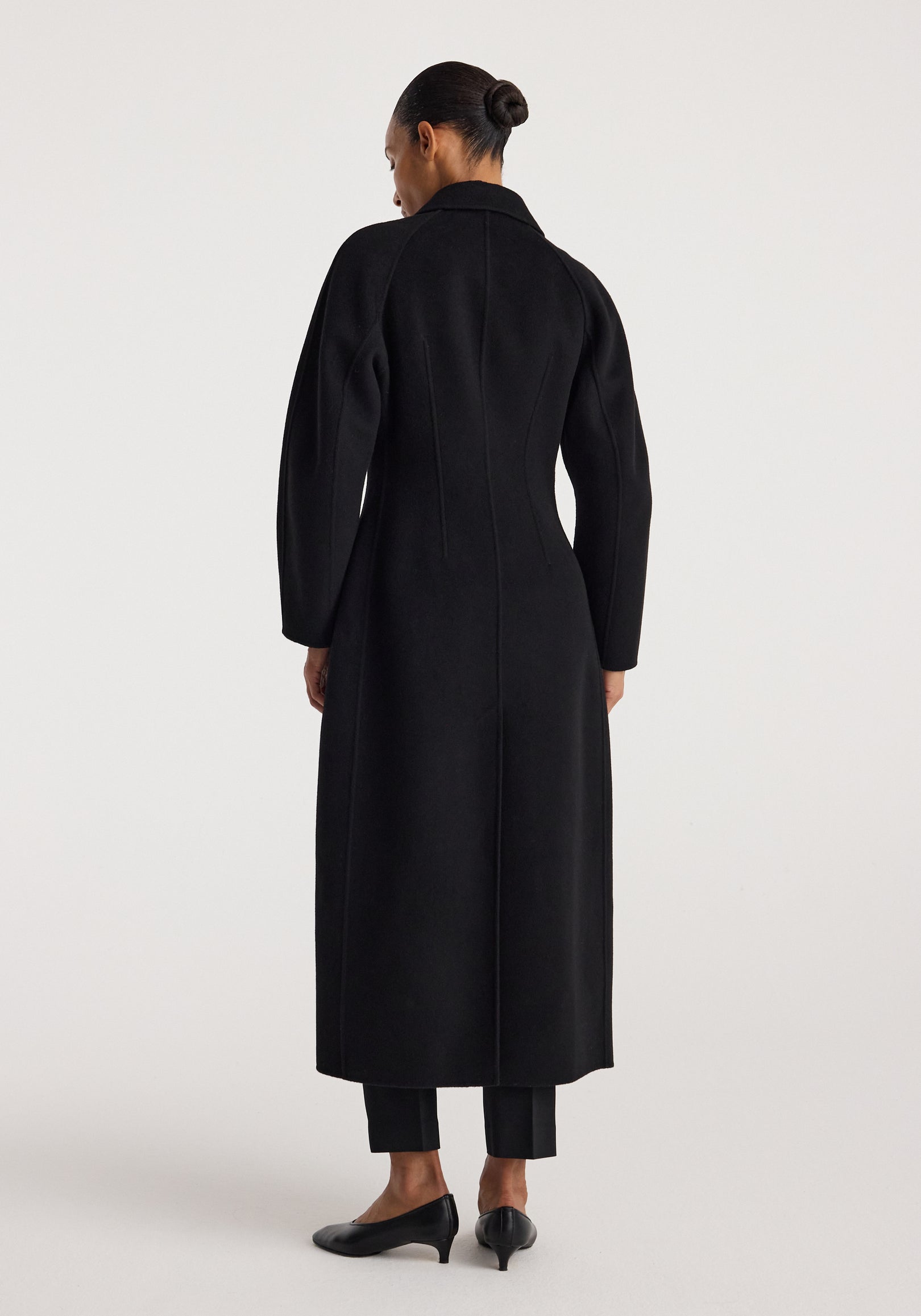 Woman modeling the Double-faced elongated sculptural coat | black, shown from the back, highlighting its long, tailored silhouette and structured design.