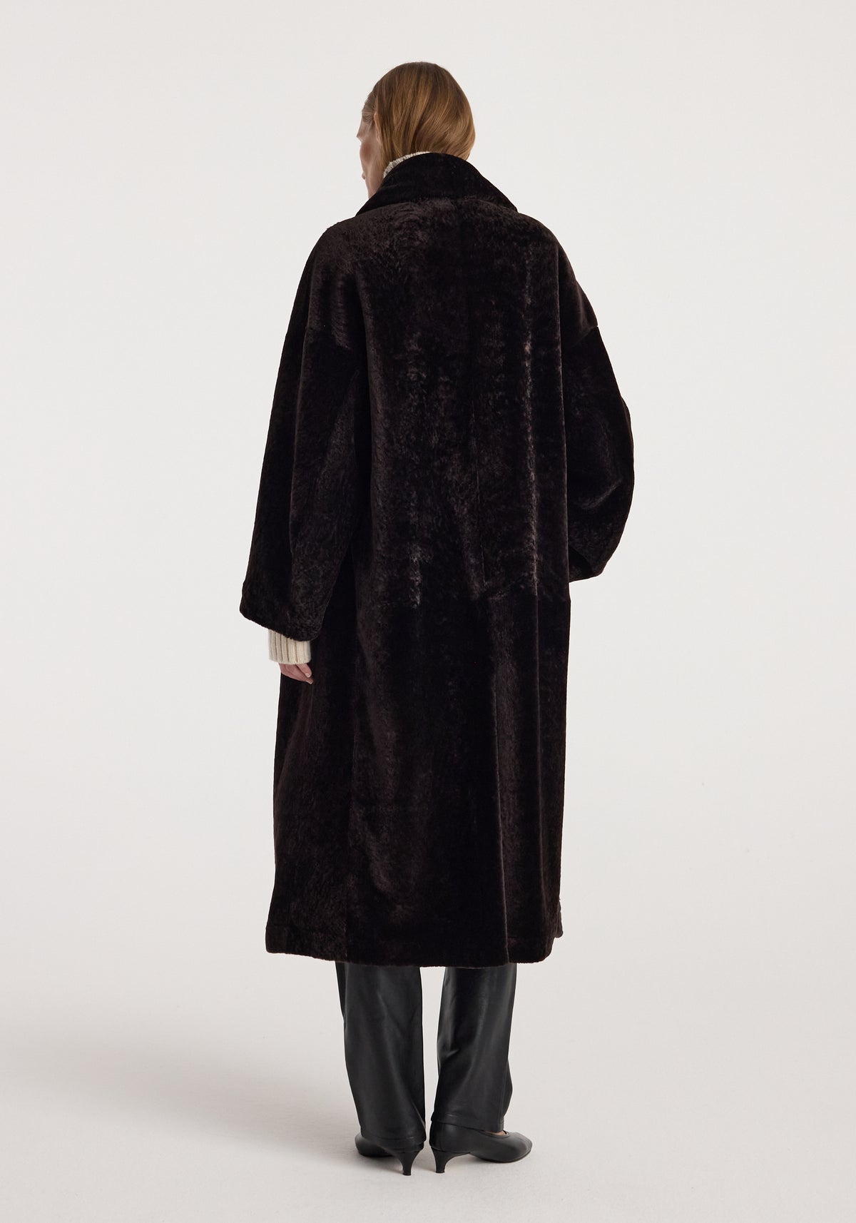 Back view of a model wearing the Shearling Shawl-Collar Coat | dark chocolate, featuring a long silhouette, plush texture, and relaxed fit.