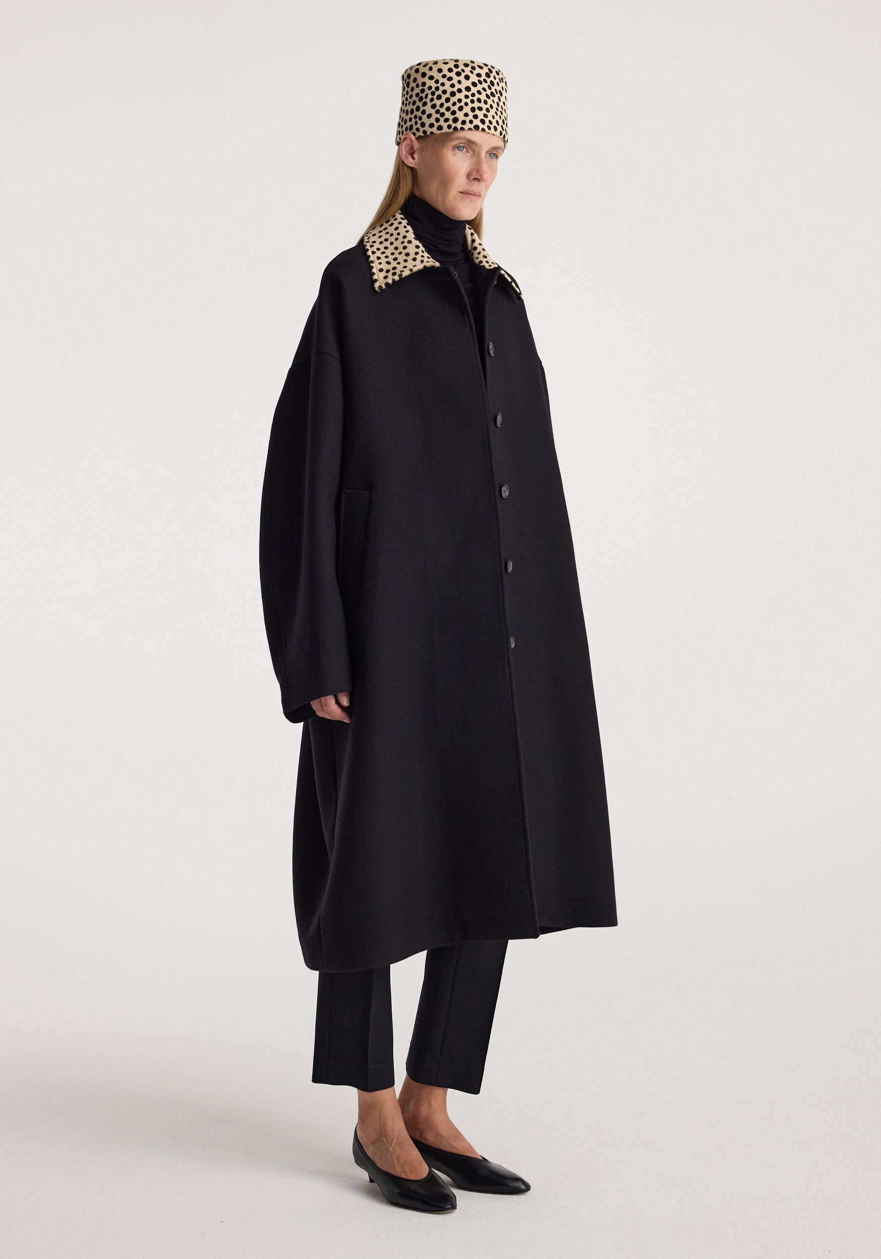 Model wearing the Cheetah collar wool coat | black with a matching cheetah print collar and hat, black trousers, and pointed black flats against a neutral background