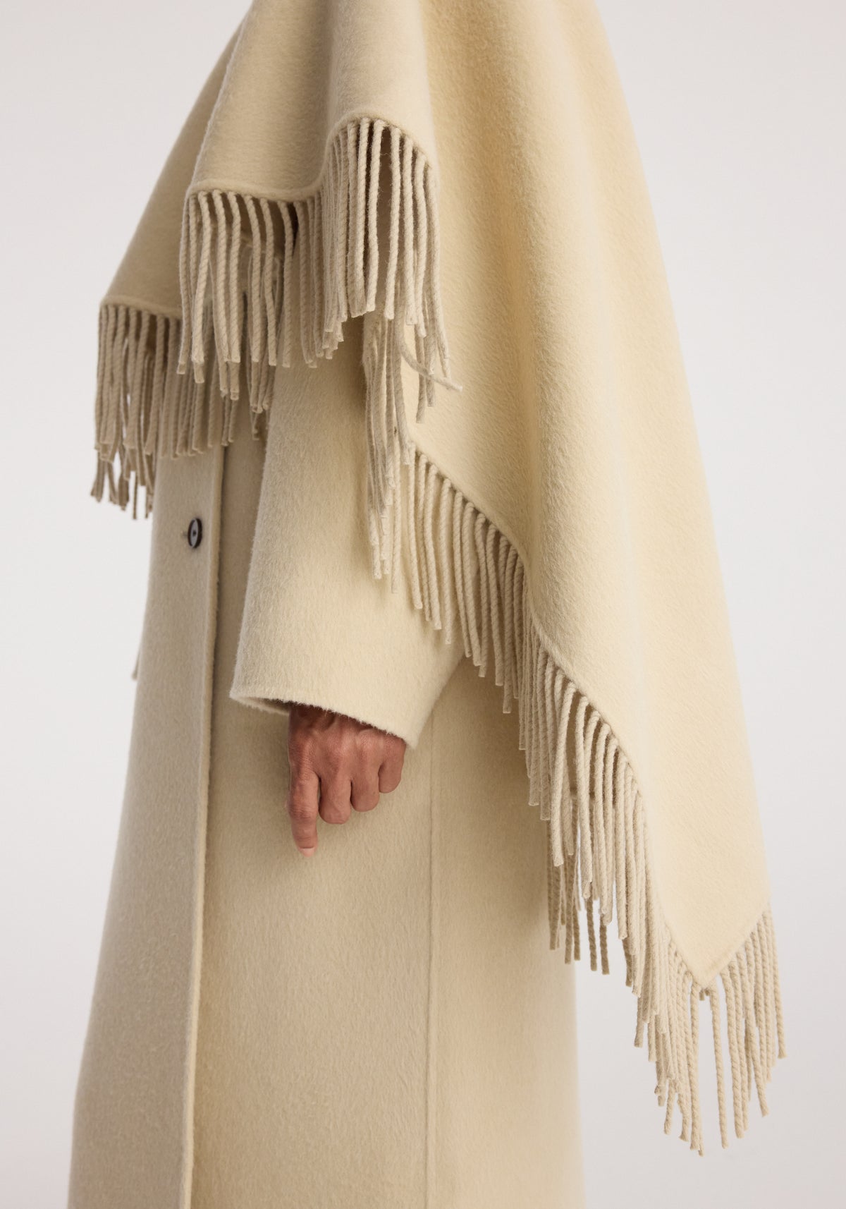 Close-up of a light butter-colored Double-faced fringe coat | butter featuring soft fabric and long fringed edges draping over the arm and side.