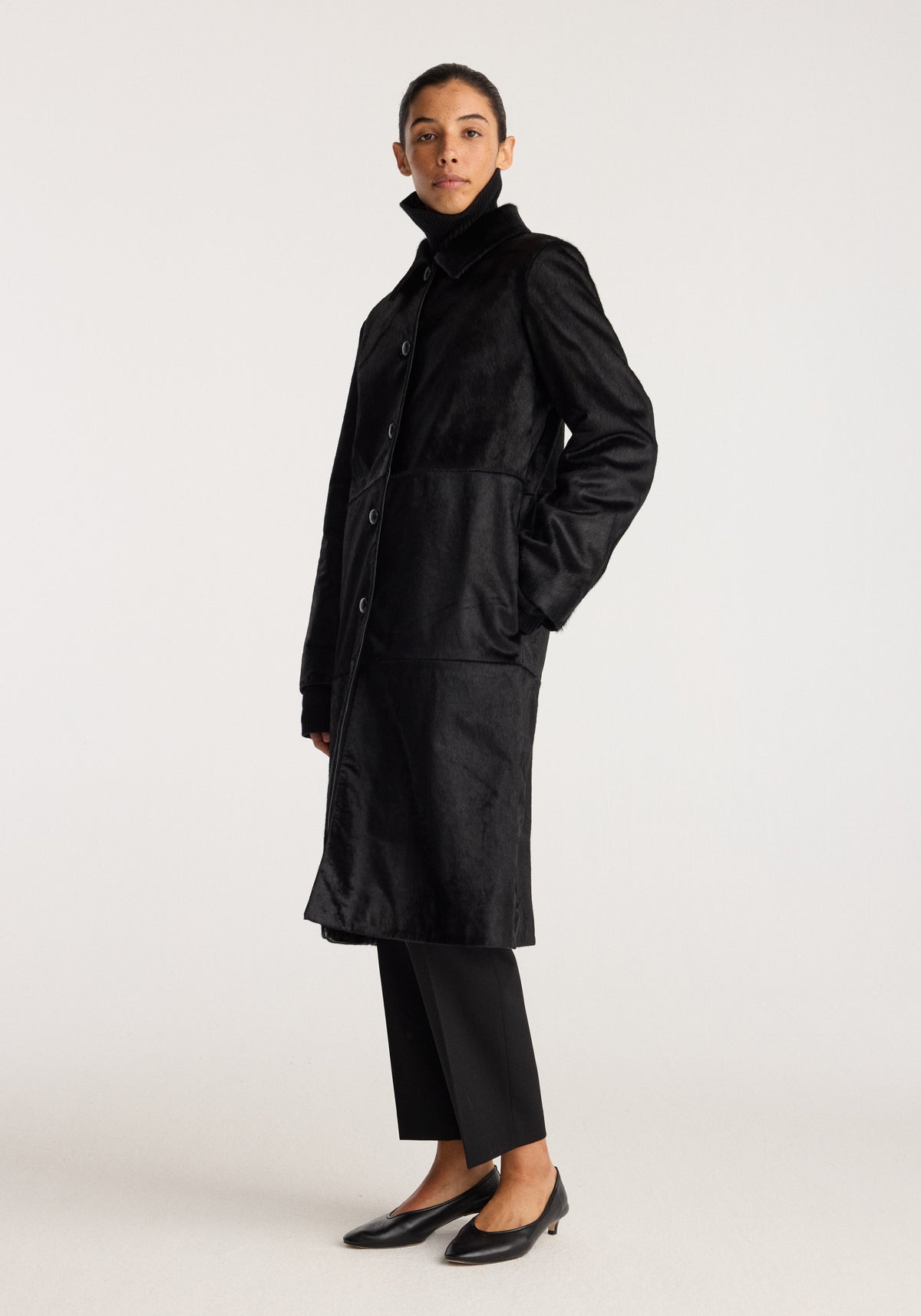 Black ponyhair coat | black shown on a model with a high collar button front and side pockets styled with black trousers and flats