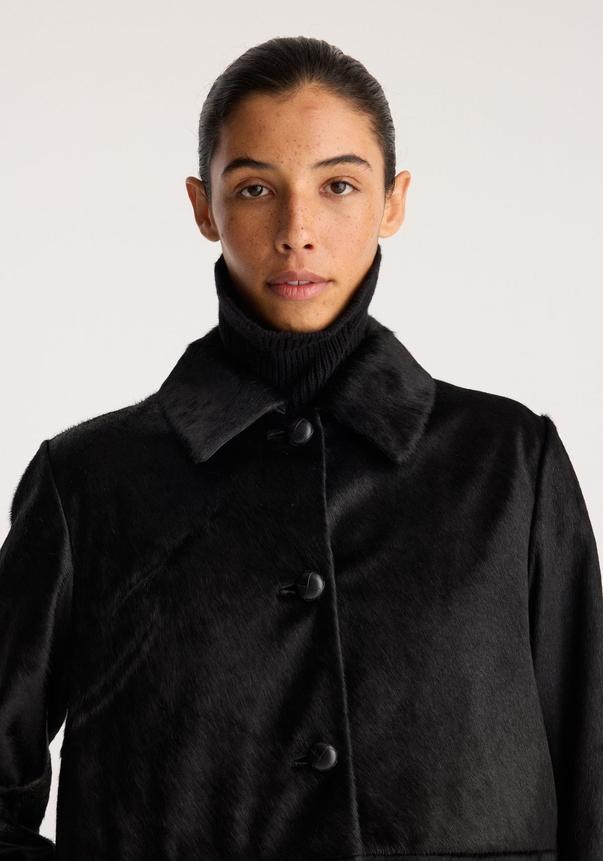Black ponyhair coat | black worn by a model with a plush texture, pointed collar, button front, and relaxed fit against a neutral background