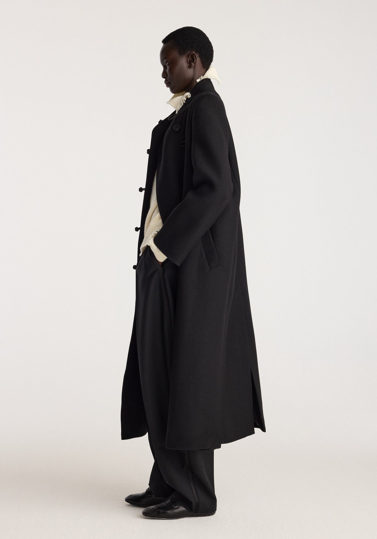 Pankou closure wool coat | black shown on a model in profile, featuring a long silhouette, toggle closures, relaxed sleeves, and side pockets