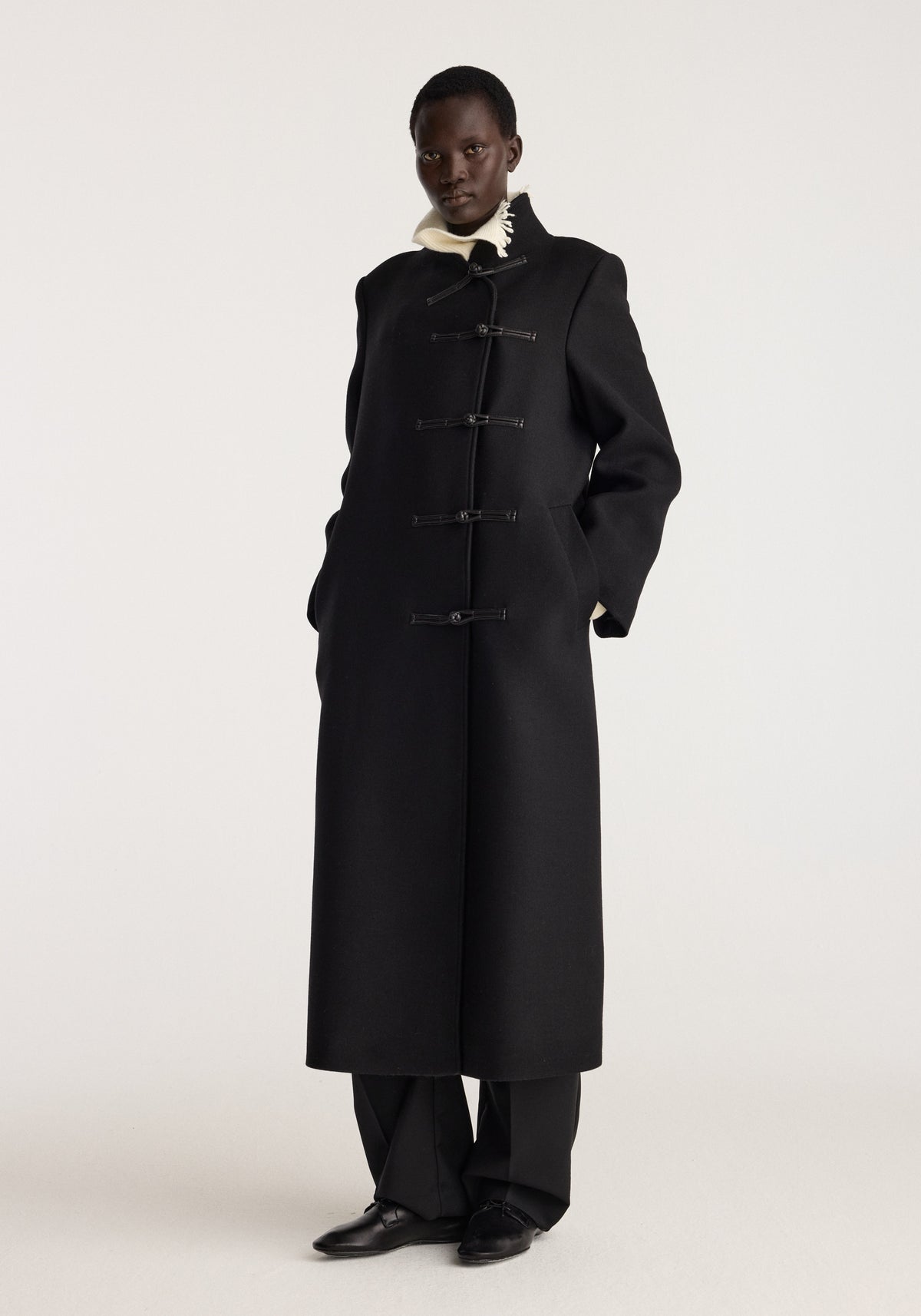 Pankou closure wool coat | black shown on a model with a long silhouette toggle closures high collar and side pockets in a studio setting