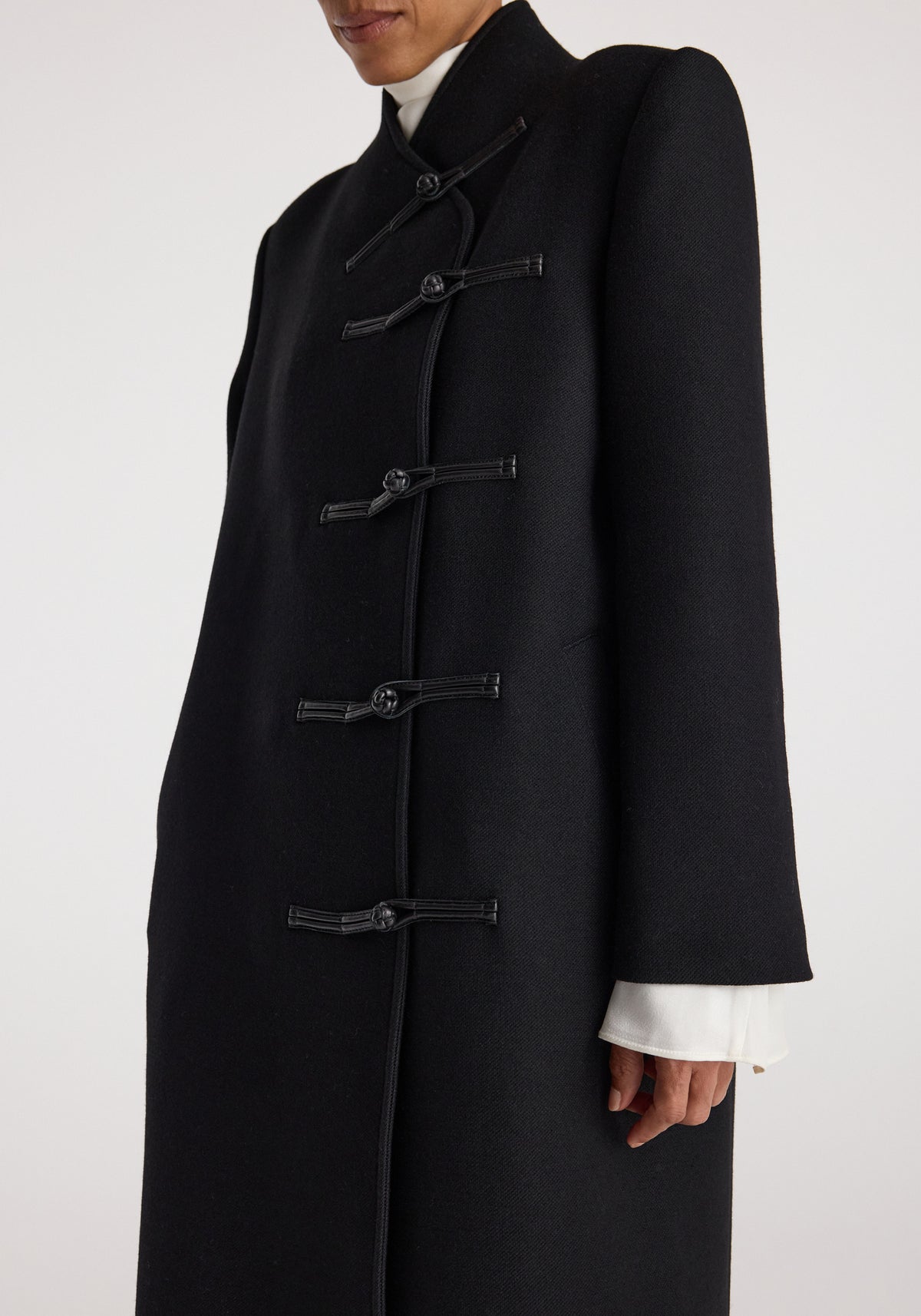 Close-up of a person wearing a Pankou closure wool coat | black, featuring traditional knot buttons and a high collar in a sleek, tailored design.
