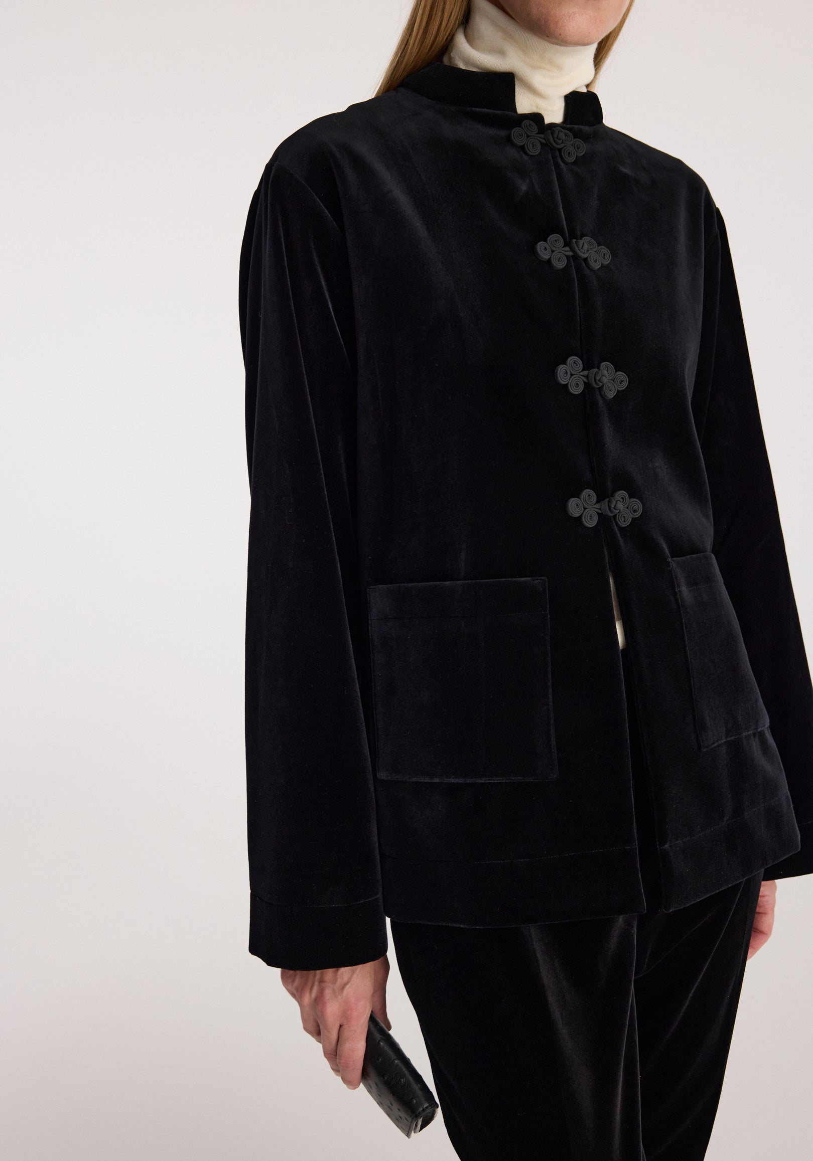 Woman wearing a black Pankou closure velvet jacket | black with a high collar, traditional knot buttons, and two front pockets, paired with matching black velvet pants.