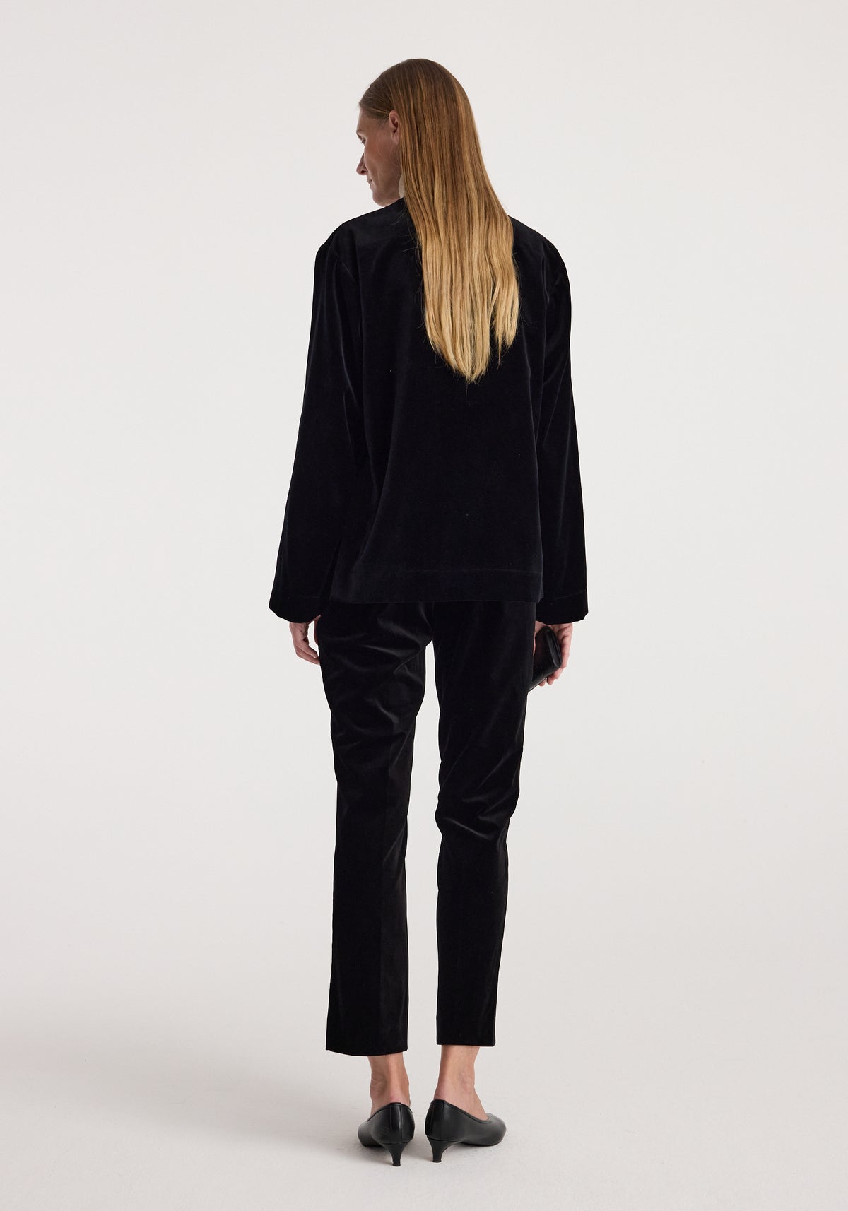 Woman wearing a black Pankou closure velvet jacket | black, shown from the back, paired with matching velvet pants and black heeled shoes.