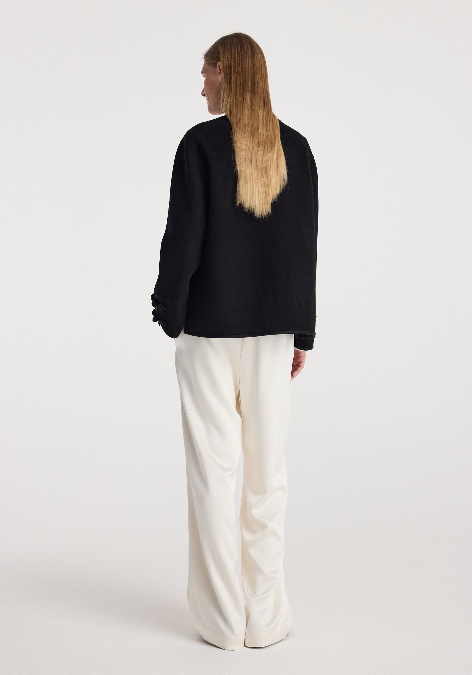 Woman wearing a black Double-faced pankou jacket | black, shown from the back, paired with loose-fitting white pants against a plain background.