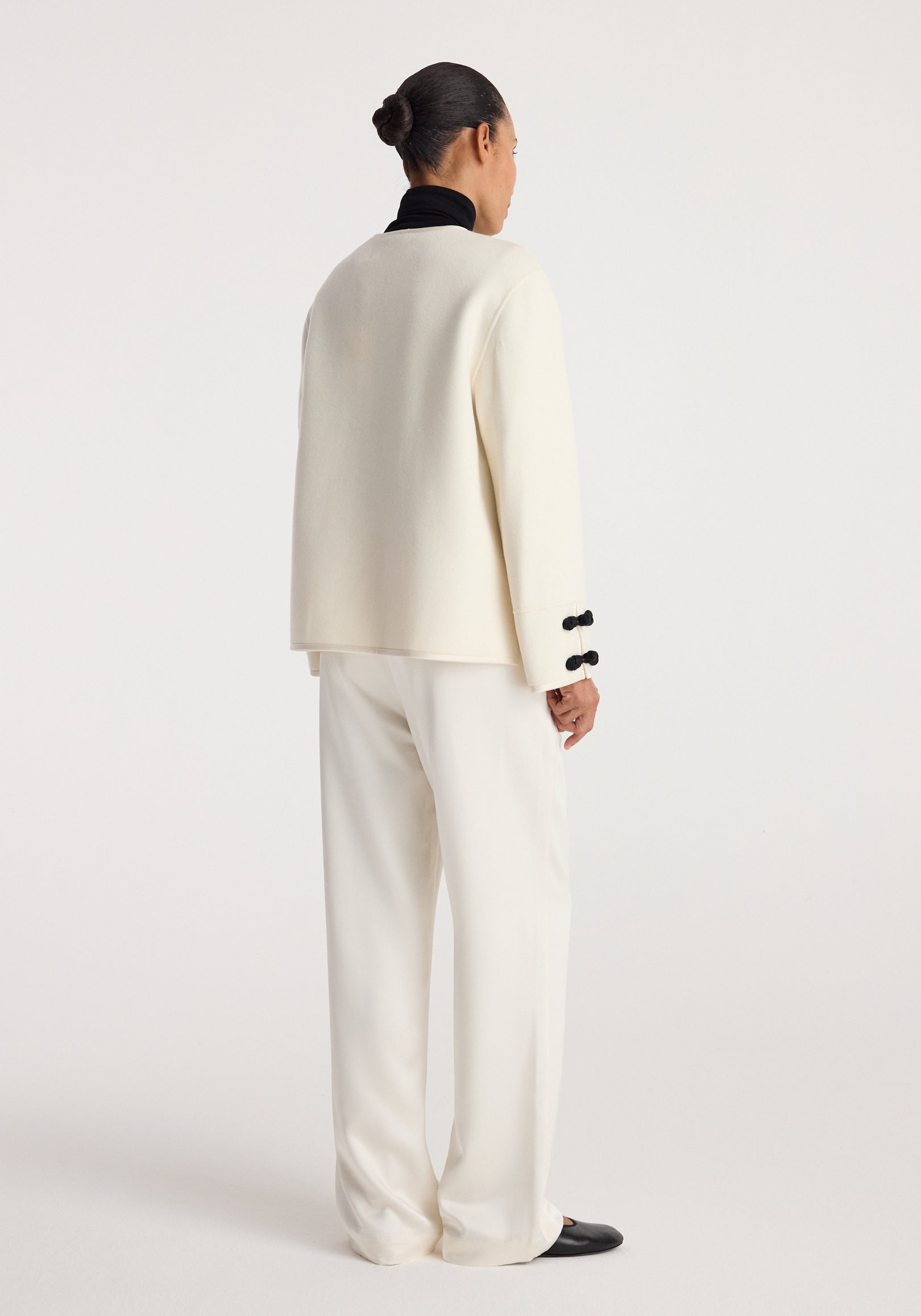 Rear view of a person wearing a Double-faced pankou jacket | off white paired with matching off-white pants and black shoes, standing against a plain background.