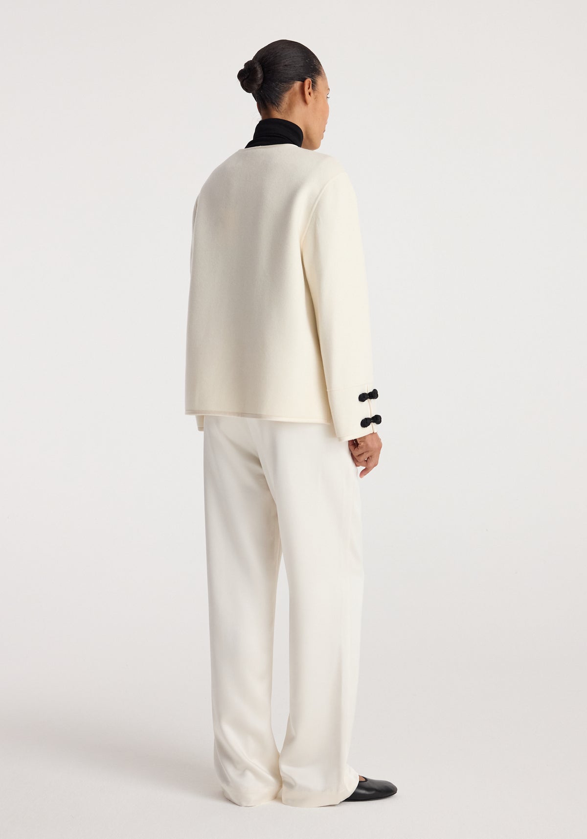 Rear view of a person wearing a Double-faced pankou jacket | off white paired with matching off-white pants and black shoes, standing against a plain background.
