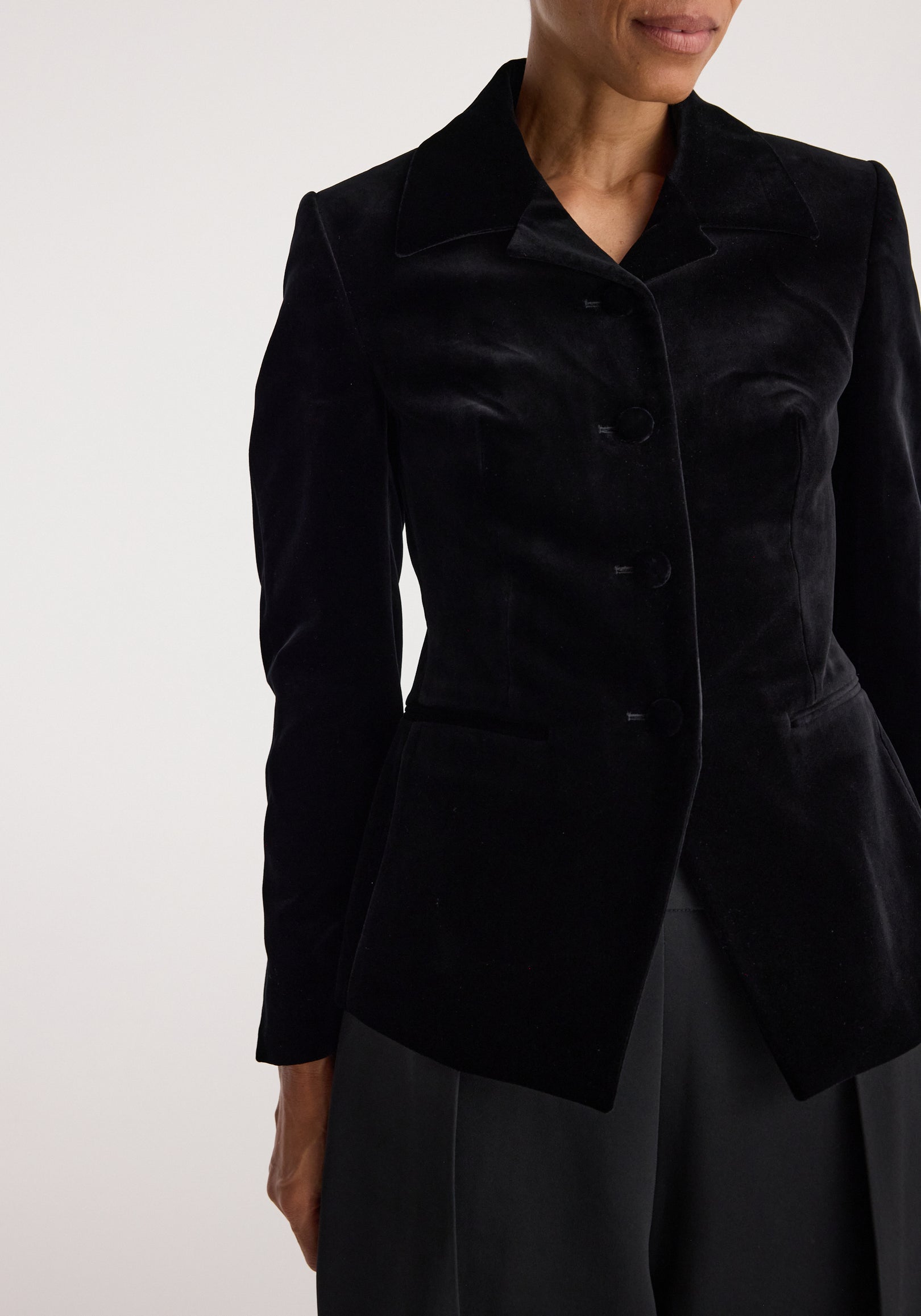 Woman wearing a fitted black velvet blazer with classic collar and button closure, styled with dark pants, showcasing the Classic fitted velvet blazer | black.