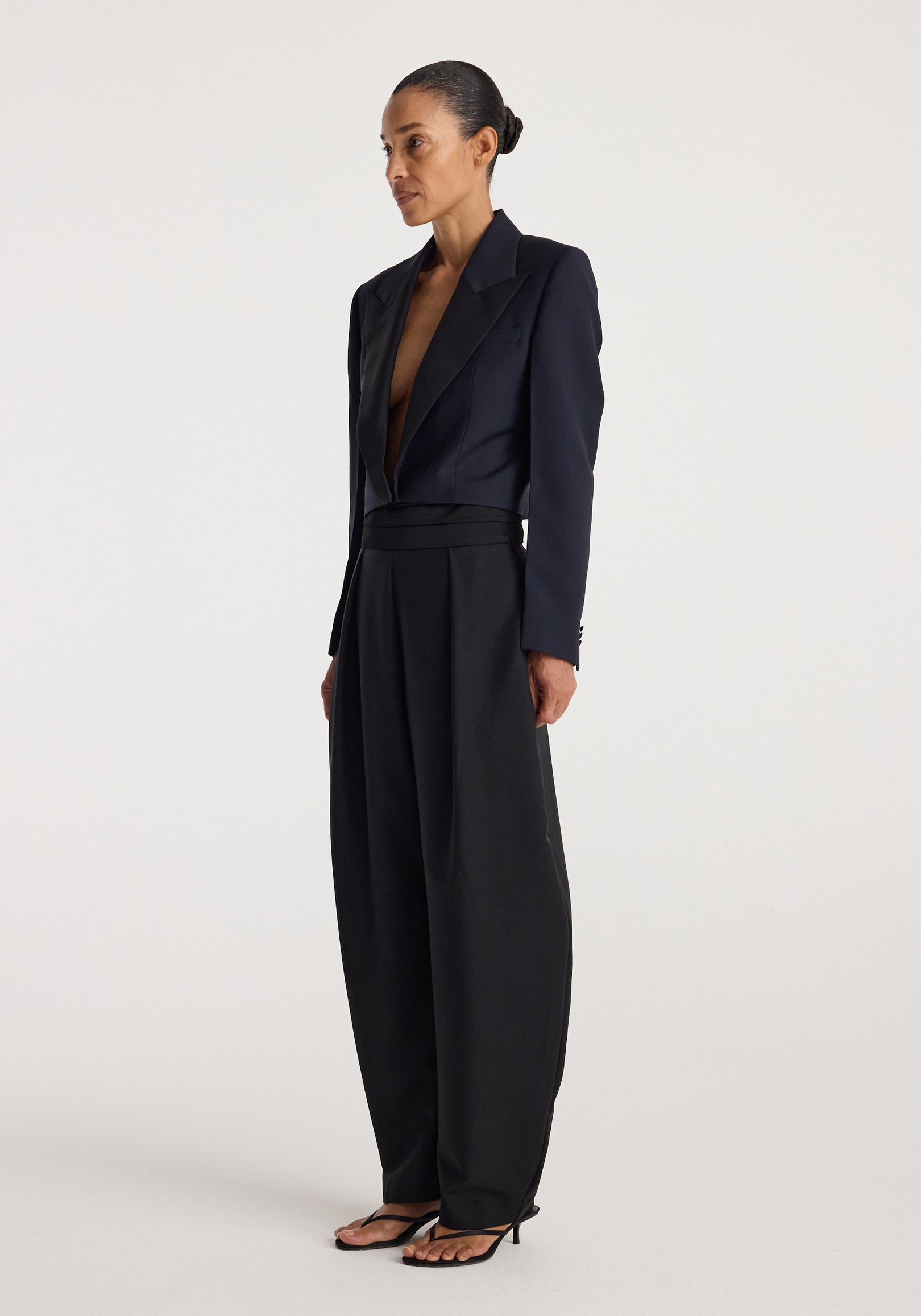 Woman wearing a navy cropped blazer with a deep V neckline paired with high-waisted wide-leg black pants and black open-toe heels, standing against a plain background.