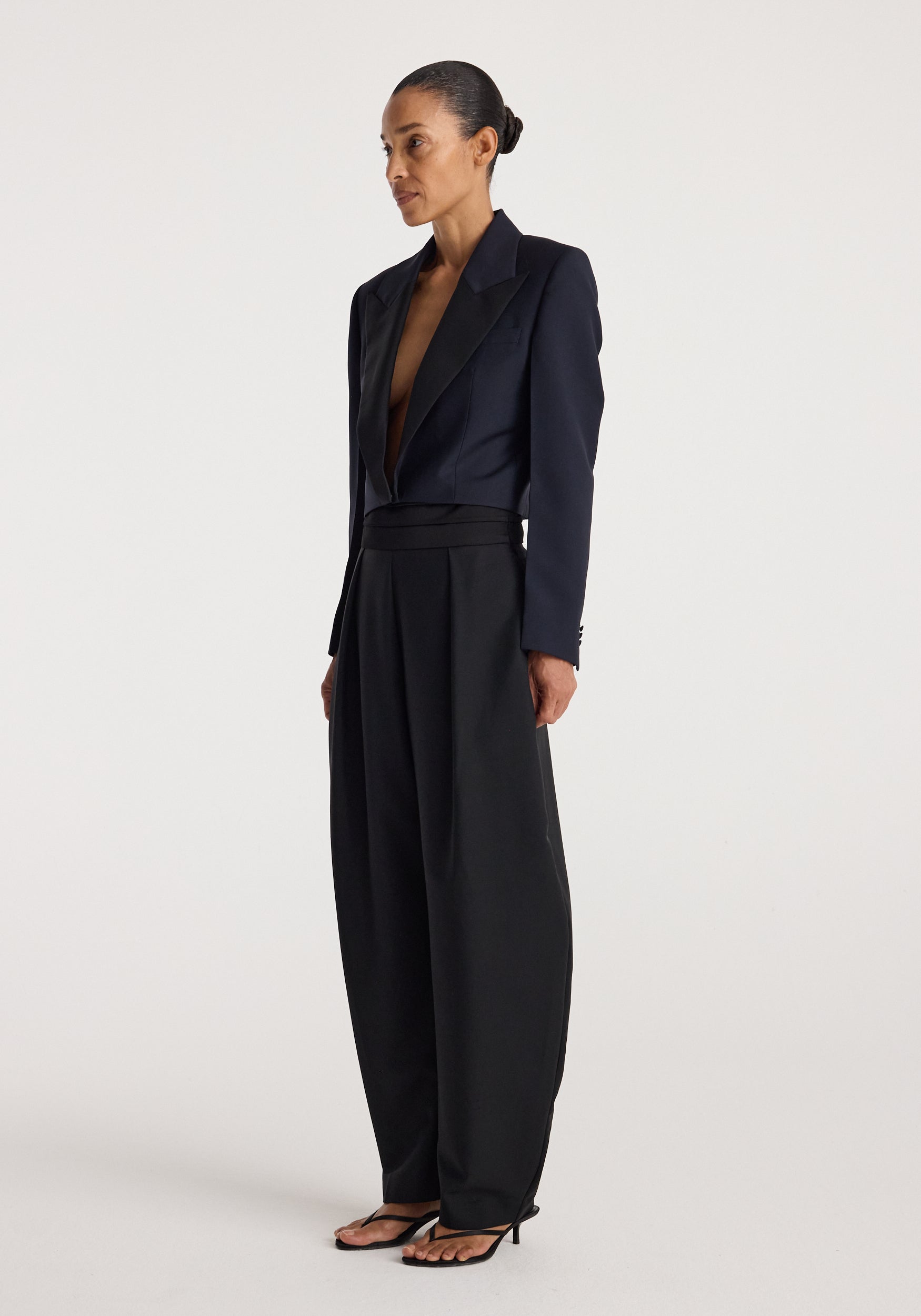 Woman wearing a navy cropped blazer with a deep V neckline paired with high-waisted wide-leg black pants and black open-toe heels, standing against a plain background.