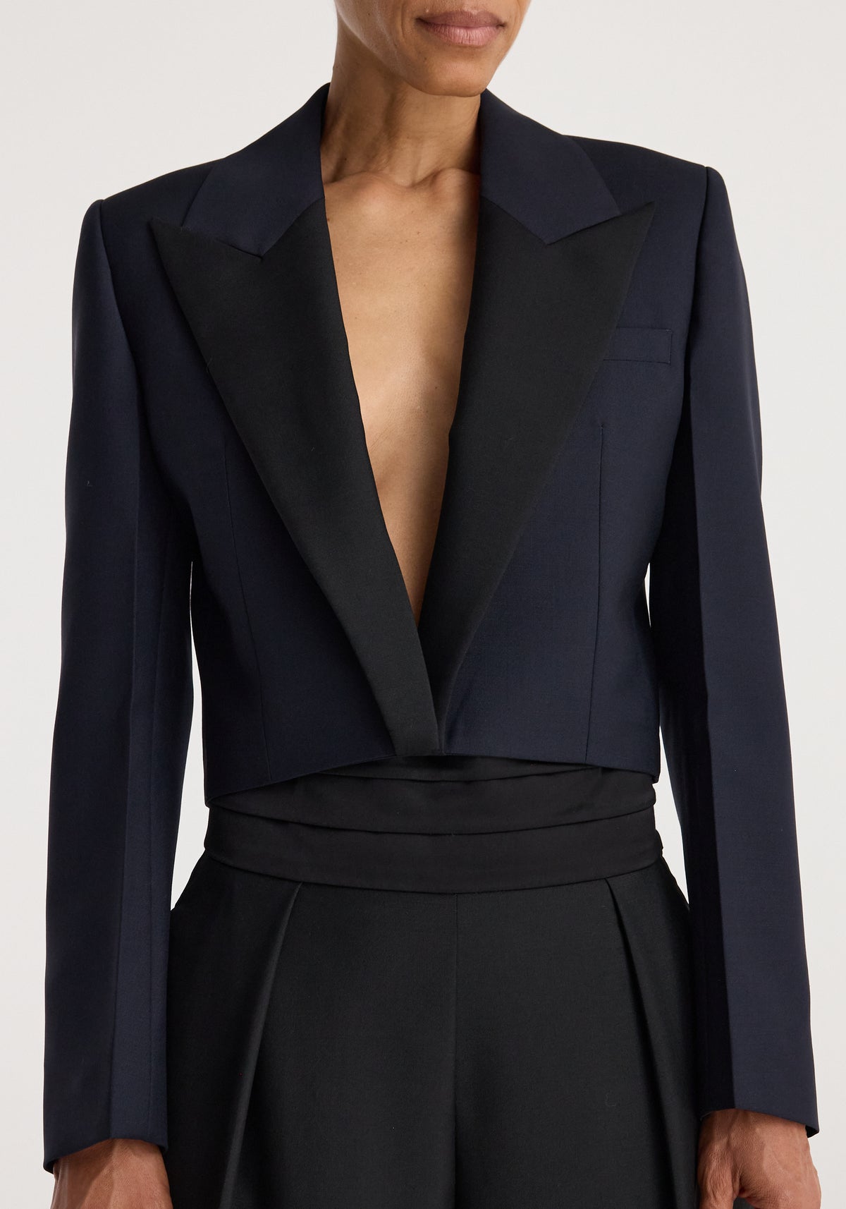 Close-up of a person wearing a tailored Cropped blazer | navy with structured shoulders and deep lapels, styled with high-waisted black pants.