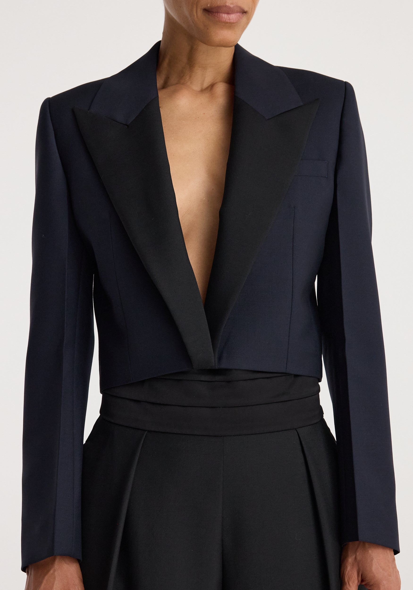 Close-up of a person wearing a tailored Cropped blazer | navy with structured shoulders and deep lapels, styled with high-waisted black pants.