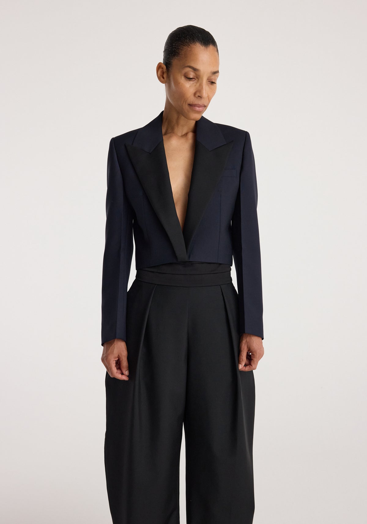 Woman wearing a tailored Cropped blazer | navy with wide lapels over high-waisted black trousers against a plain light background.