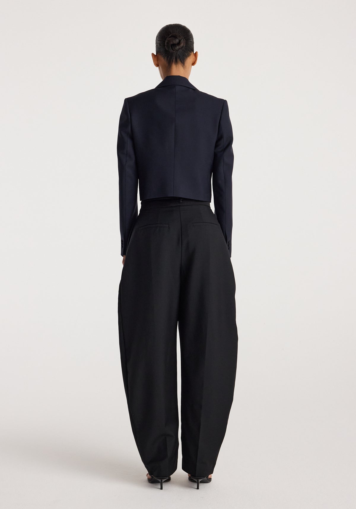 Rear view of a model wearing a cropped blazer | navy paired with wide-leg black trousers and black heels, standing against a plain light background.