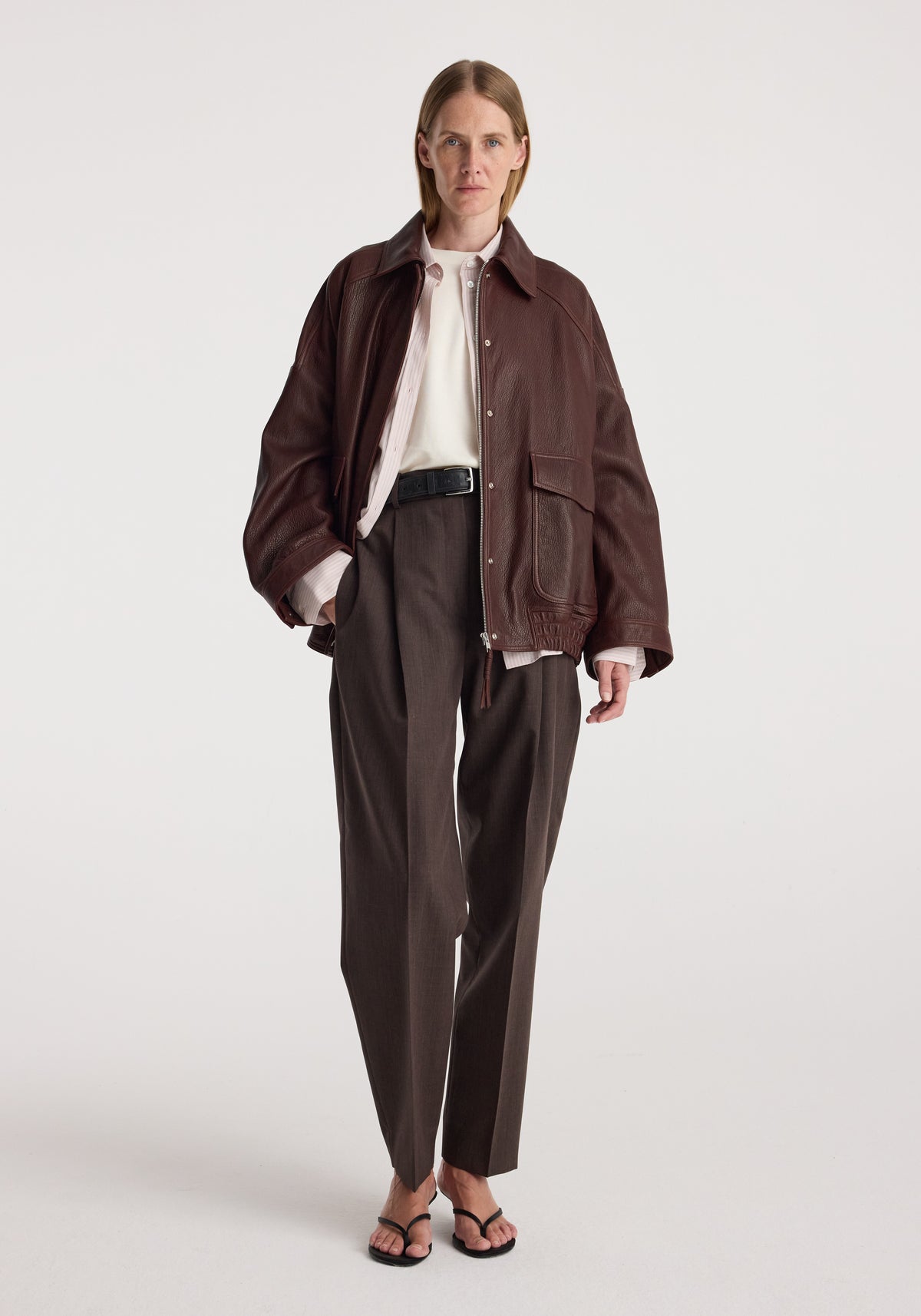 Model wearing Grain leather aviator jacket | chestnut over a white shirt with dark trousers and strappy sandals against a neutral studio background