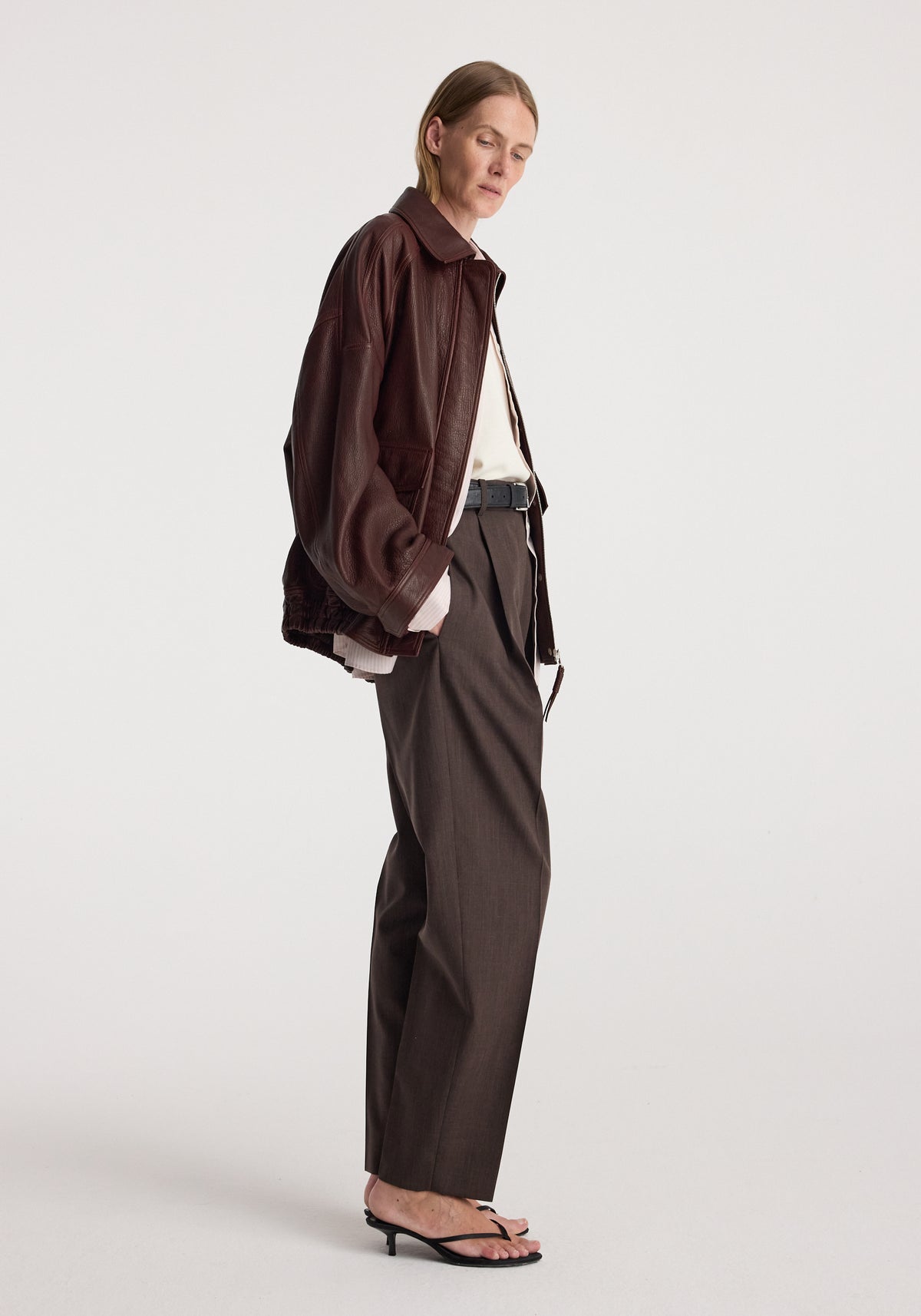 Grain leather aviator jacket | chestnut worn by a model in side profile with tailored trousers and strappy sandals against a light studio background