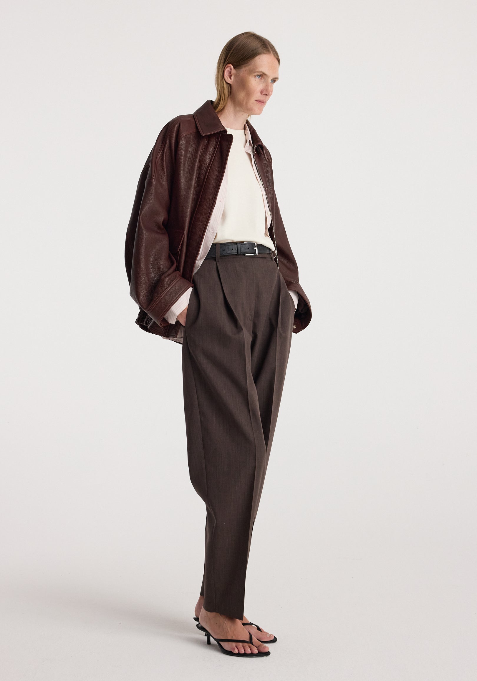 Model wearing the Grain leather aviator jacket | chestnut with a white shirt, dark tailored trousers, and sandals against a light studio background