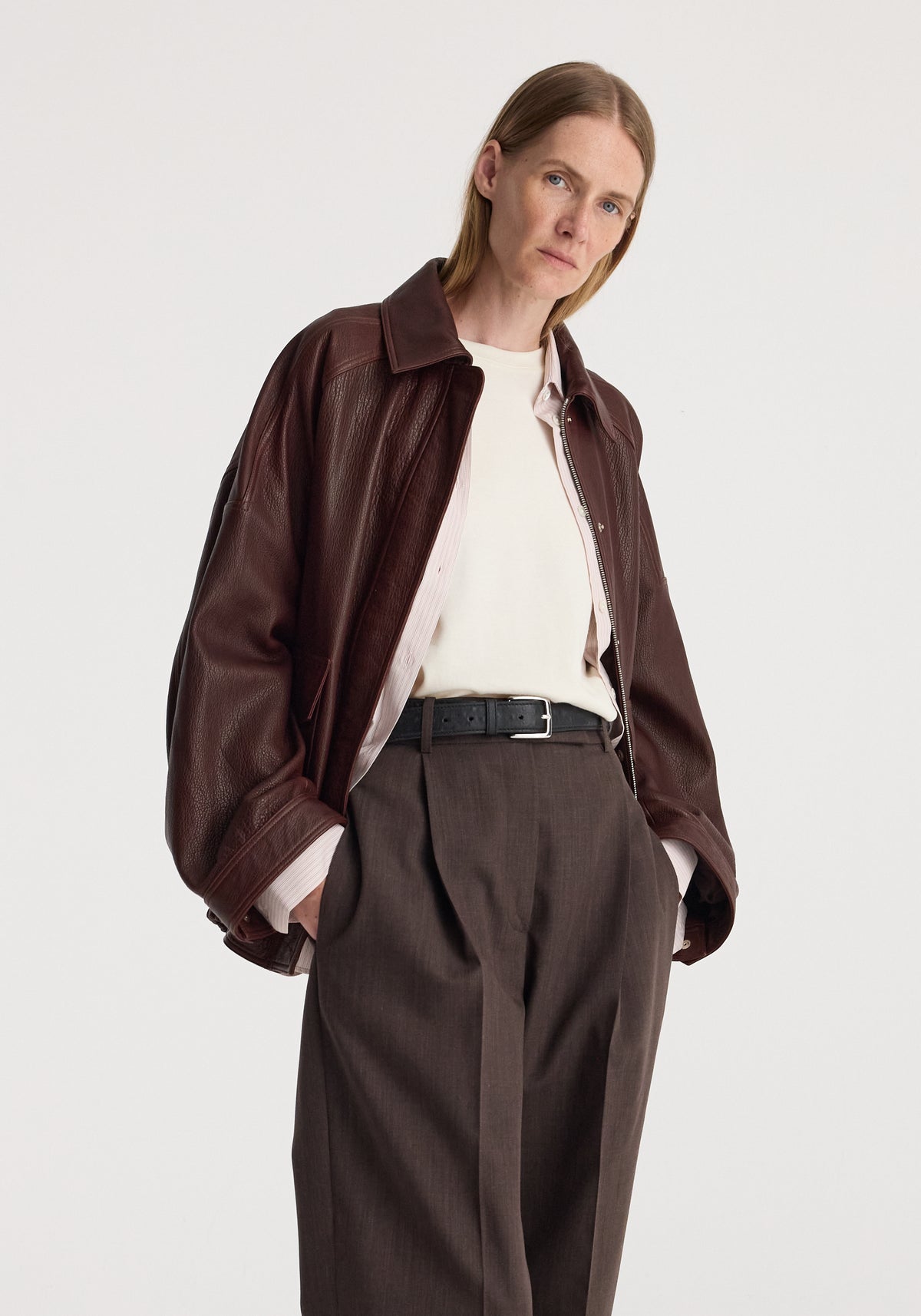 Grain leather aviator jacket | chestnut worn with a cream shirt and tailored brown trousers by a model against a light background