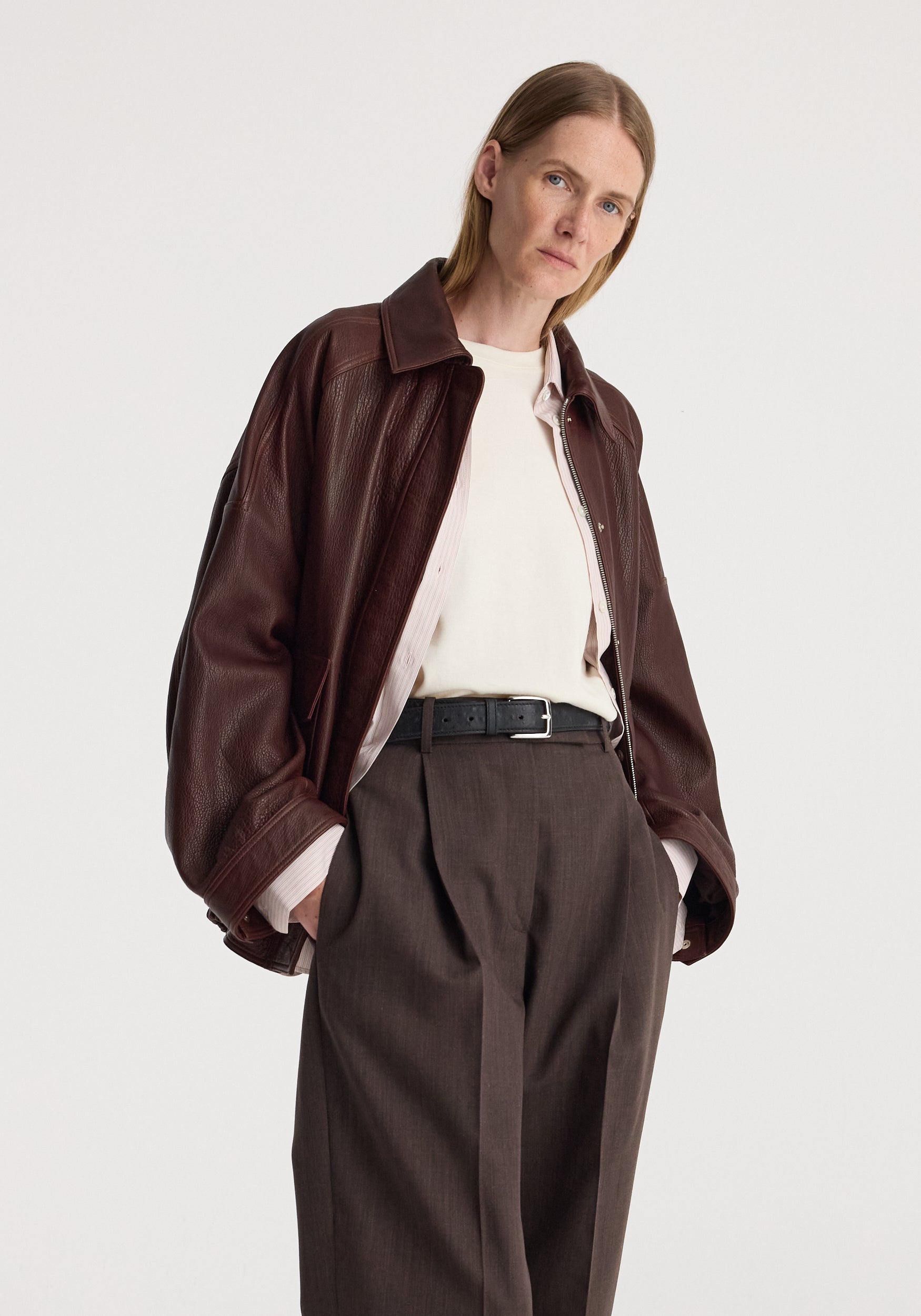 Grain leather aviator jacket | chestnut worn with a cream shirt and tailored brown trousers by a model against a light background