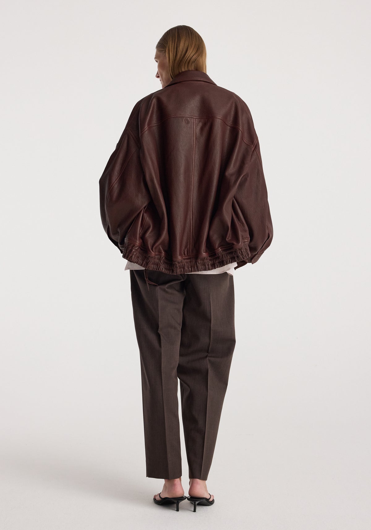 Grain leather aviator jacket | chestnut shown from the back on a model, featuring a roomy silhouette, gathered hem, and long sleeves.