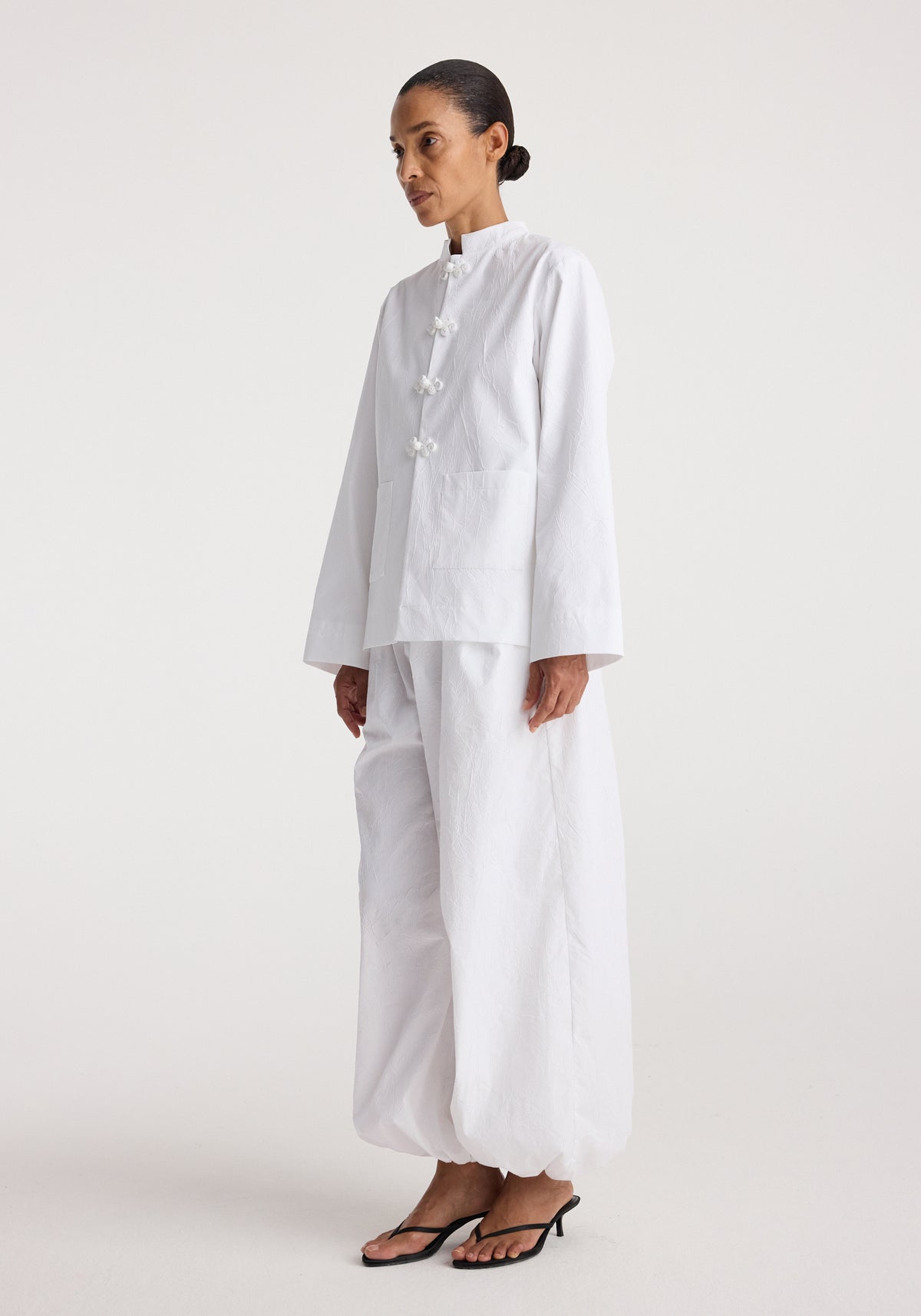Woman wearing a white Pankou closure crushed jacket | optic white with long sleeves and loose fit, paired with matching wide-leg pants and black heeled sandals.
