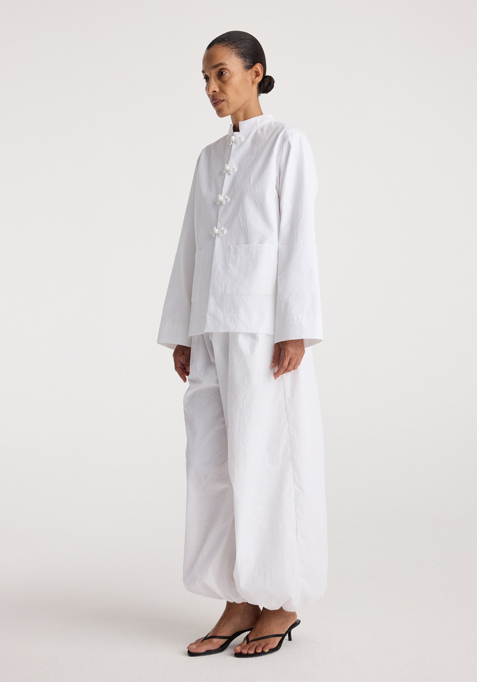 Woman wearing a white Pankou closure crushed jacket | optic white with long sleeves and loose fit, paired with matching wide-leg pants and black heeled sandals.