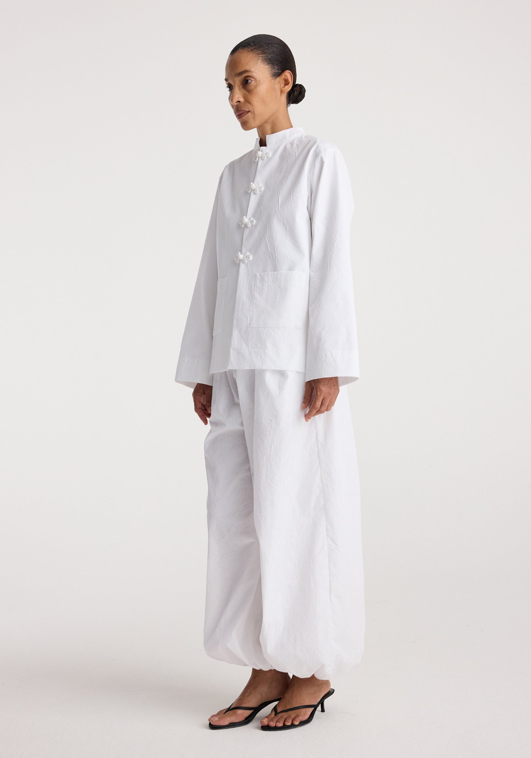 Woman wearing a white Pankou closure crushed jacket | optic white with long sleeves and loose fit, paired with matching wide-leg pants and black heeled sandals.