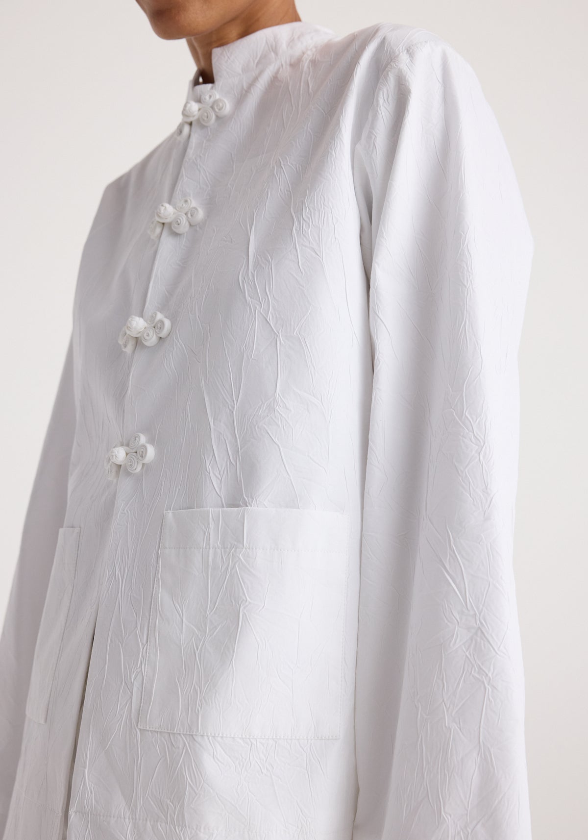 Close-up of a person wearing a Pankou closure crushed jacket | optic white with textured fabric, featuring traditional knot buttons and front pockets.