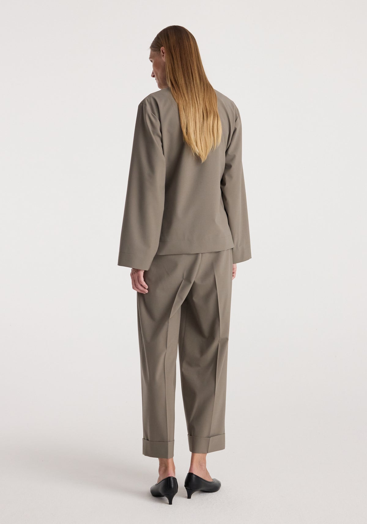 Pankou closure jacket | taupe shown from the back on a model wearing matching taupe trousers and black heeled shoes against a light studio background