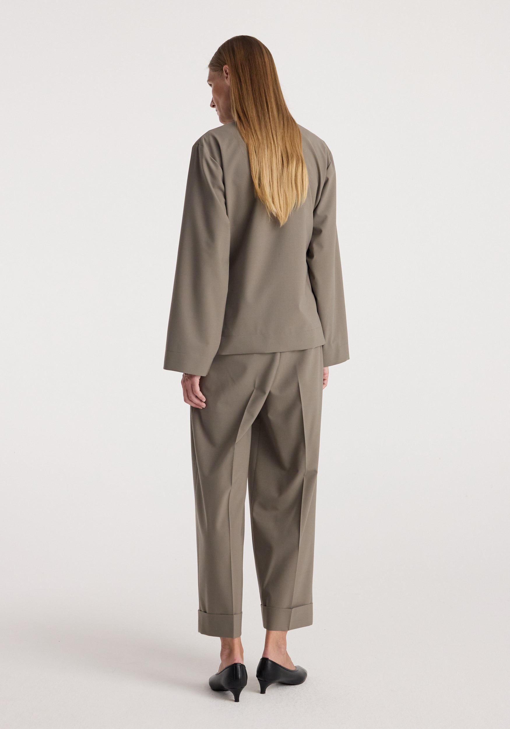 Pankou closure jacket | taupe shown from the back on a model wearing matching taupe trousers and black heeled shoes against a light studio background