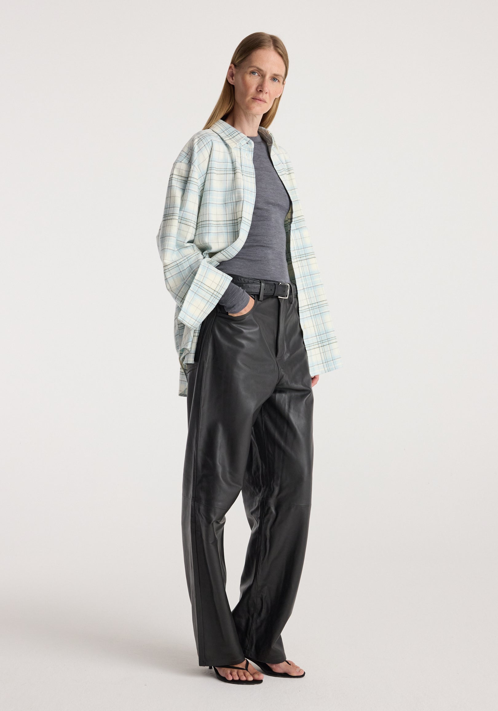 Flannel check overshirt | sea green check worn open by a woman with a grey top, black leather trousers and sandals in a studio setting