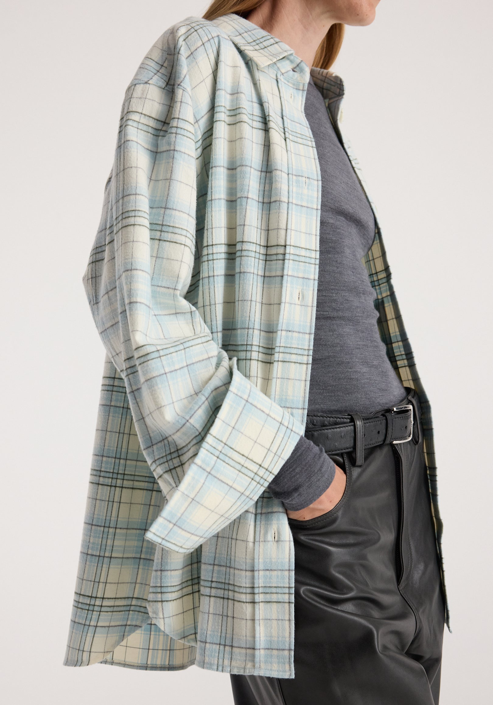 Flannel check overshirt | sea green check worn open by a woman over a dark top, with rolled sleeves and black trousers.