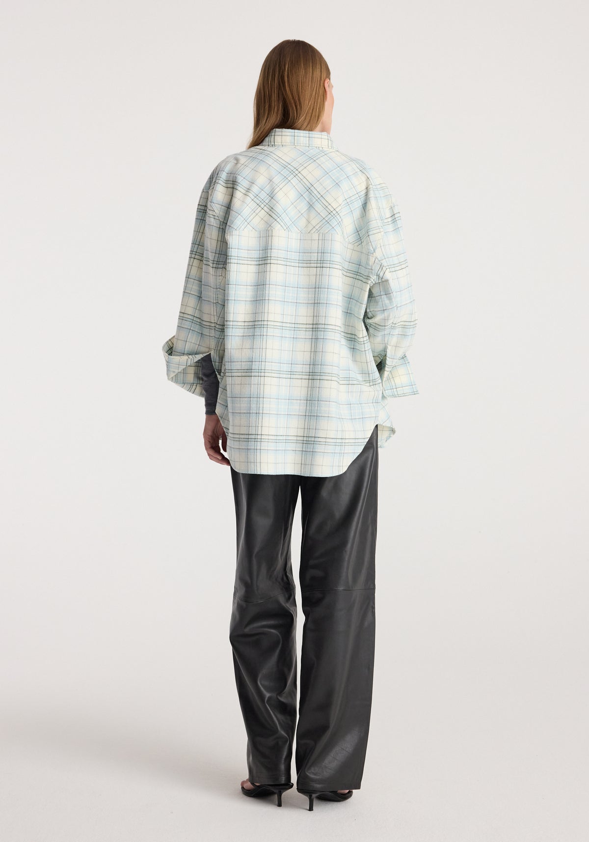 Back view of model wearing Flannel check overshirt | sea green check, a relaxed pale green plaid shirt with rolled sleeves and black trousers
