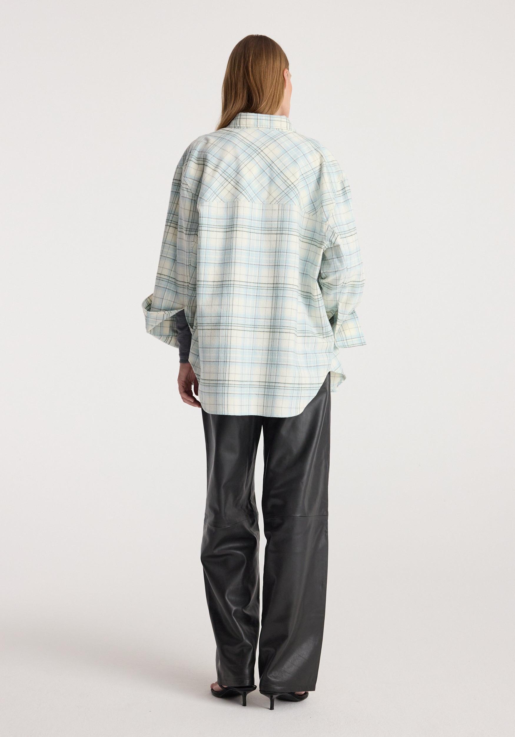 Back view of model wearing Flannel check overshirt | sea green check, a relaxed pale green plaid shirt with rolled sleeves and black trousers