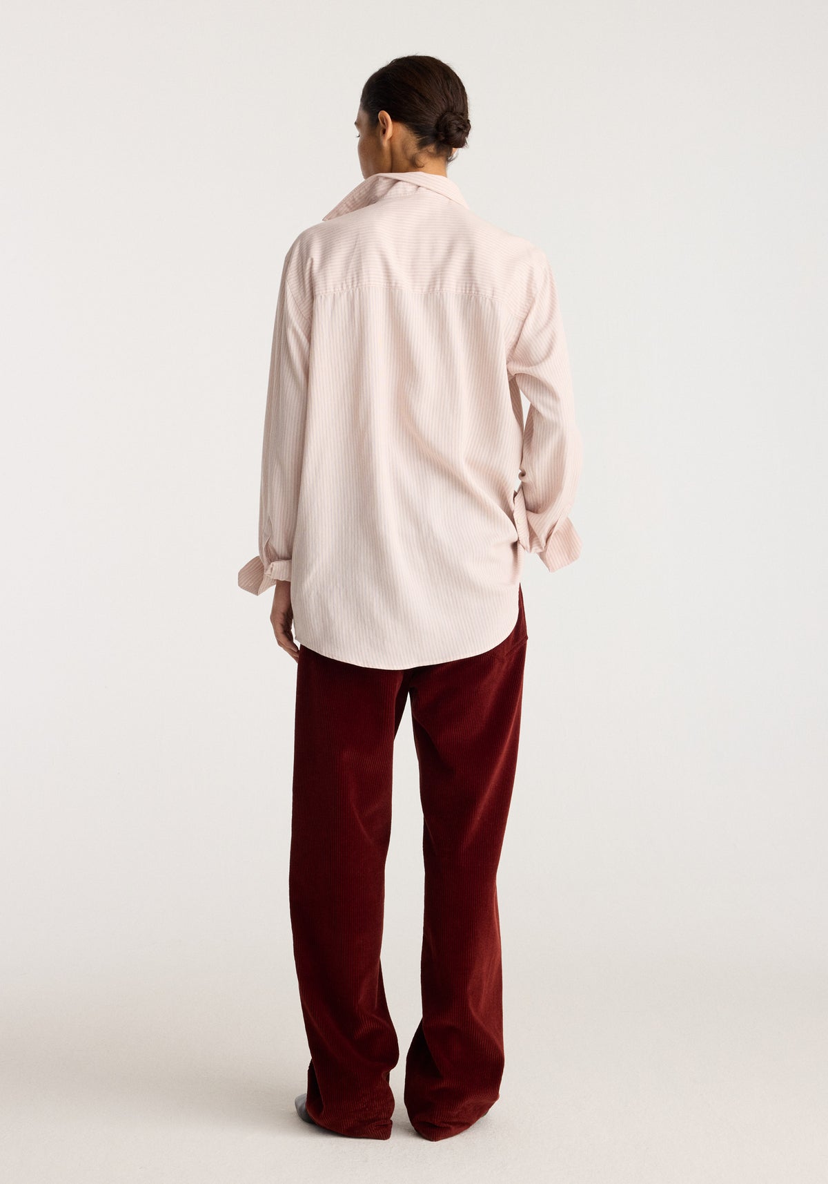Classic fit striped shirt | rose stripe shown from the back on a model with long sleeves and a curved hem in soft rose stripes over burgundy trousers