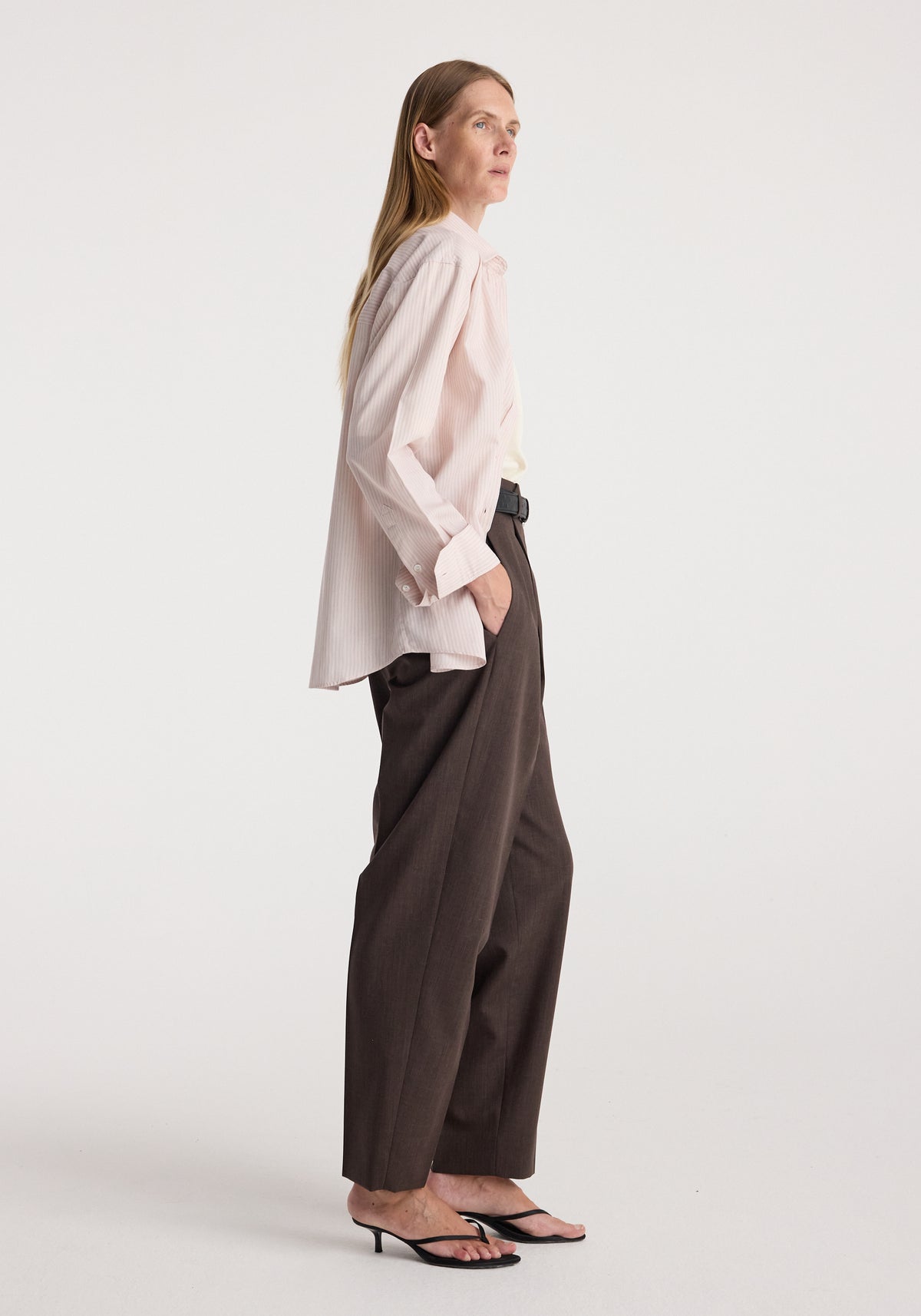 Woman wearing a Classic fit striped shirt | rose stripe, featuring a relaxed fit with long sleeves and subtle rose stripes, paired with dark wide-leg trousers and black heeled sandals.