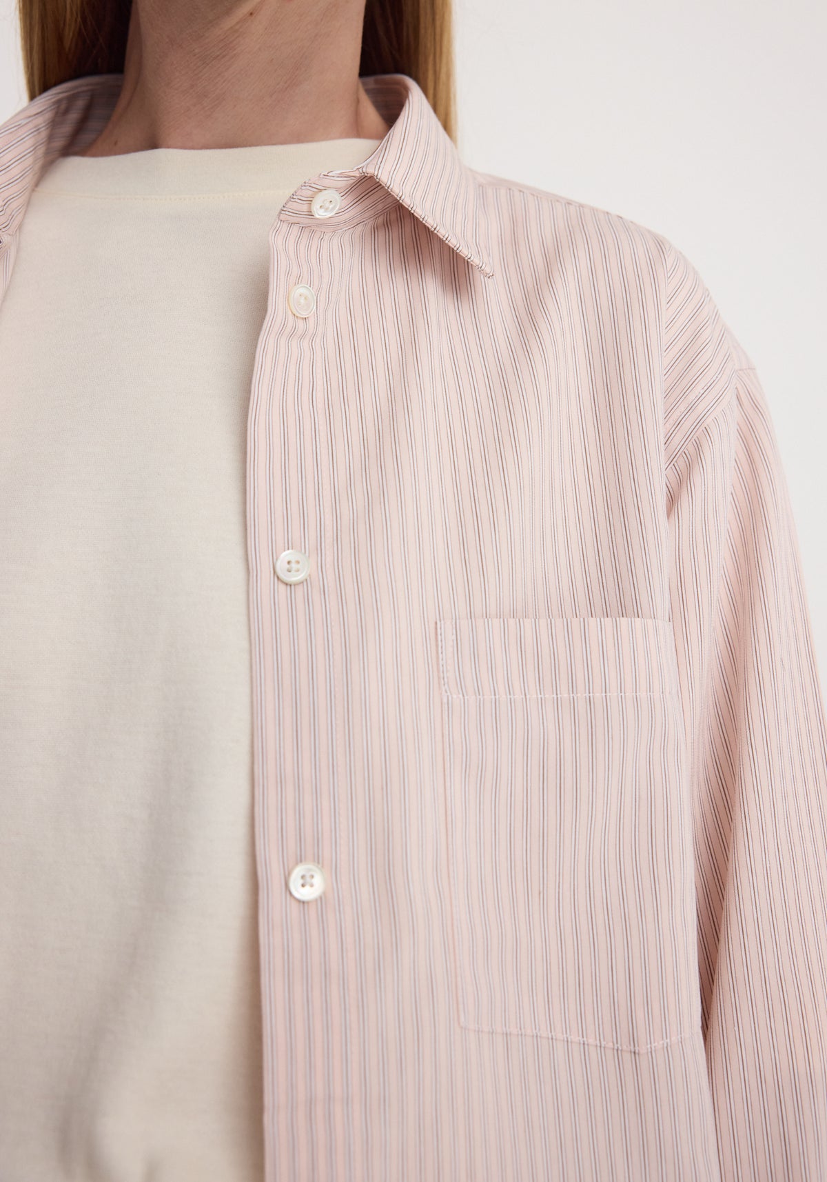 Close-up of a person wearing a classic fit striped shirt | rose stripe with thin vertical stripes in soft pink and white buttons over a plain white undershirt.