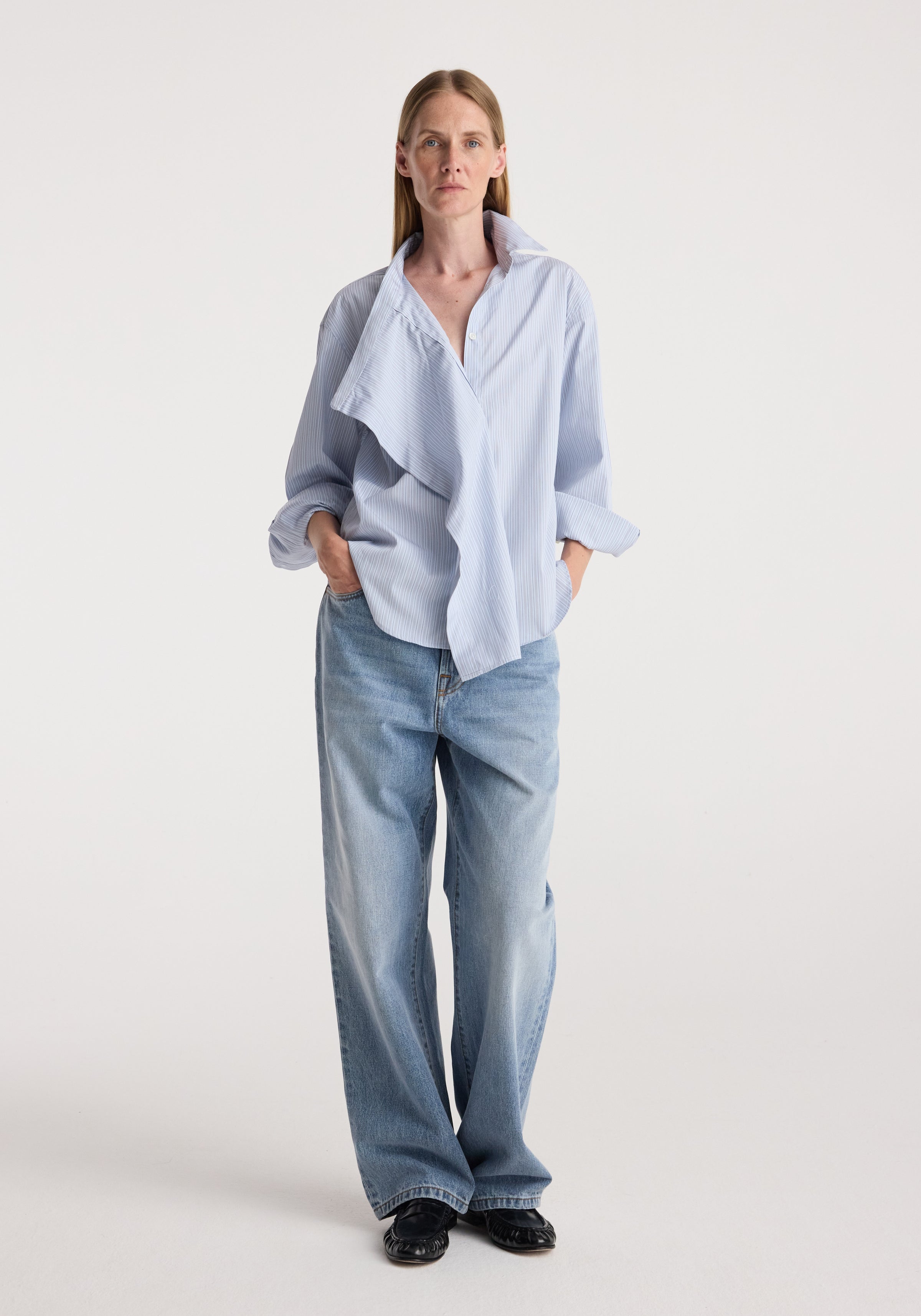 Draped collar shirt | blue stripe worn by a woman with rolled sleeves, relaxed fit, light wash jeans, and black shoes against a neutral studio background