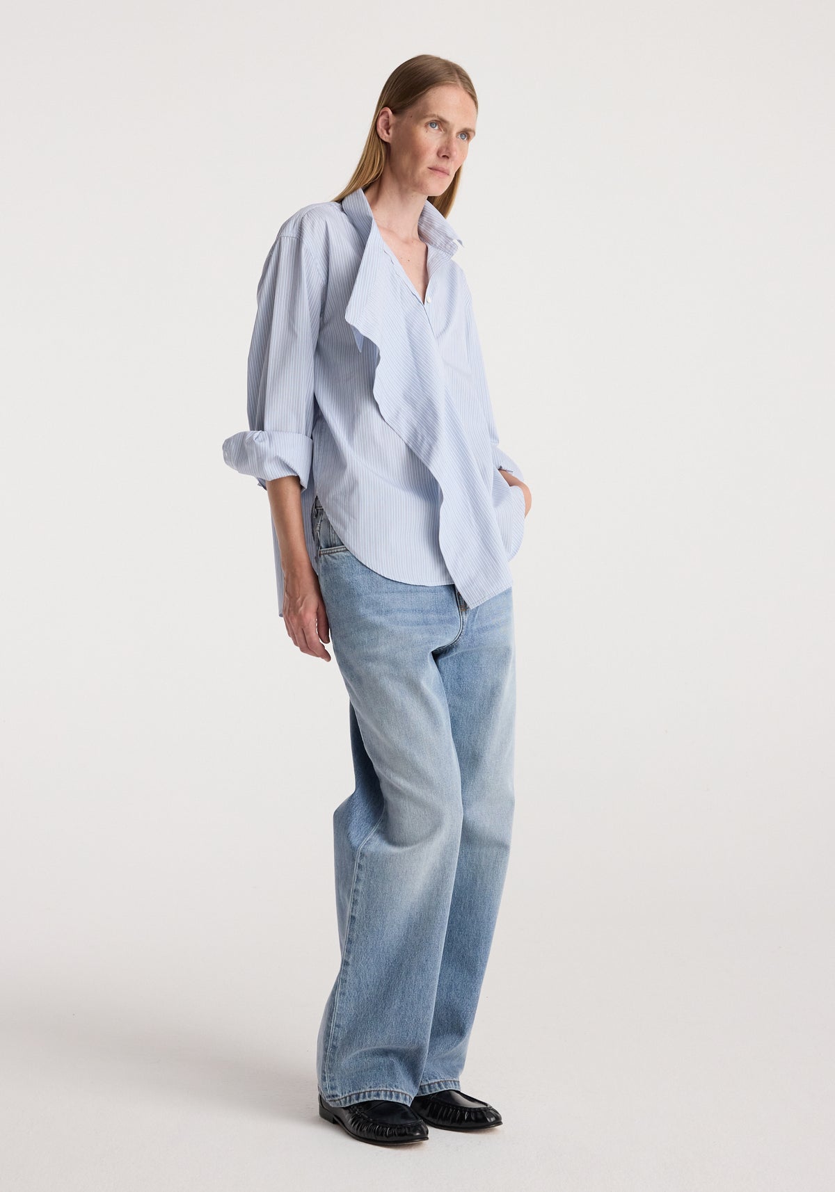 Draped collar shirt | blue stripe worn by a woman with rolled sleeves, paired with relaxed light wash jeans and black shoes in a studio setting