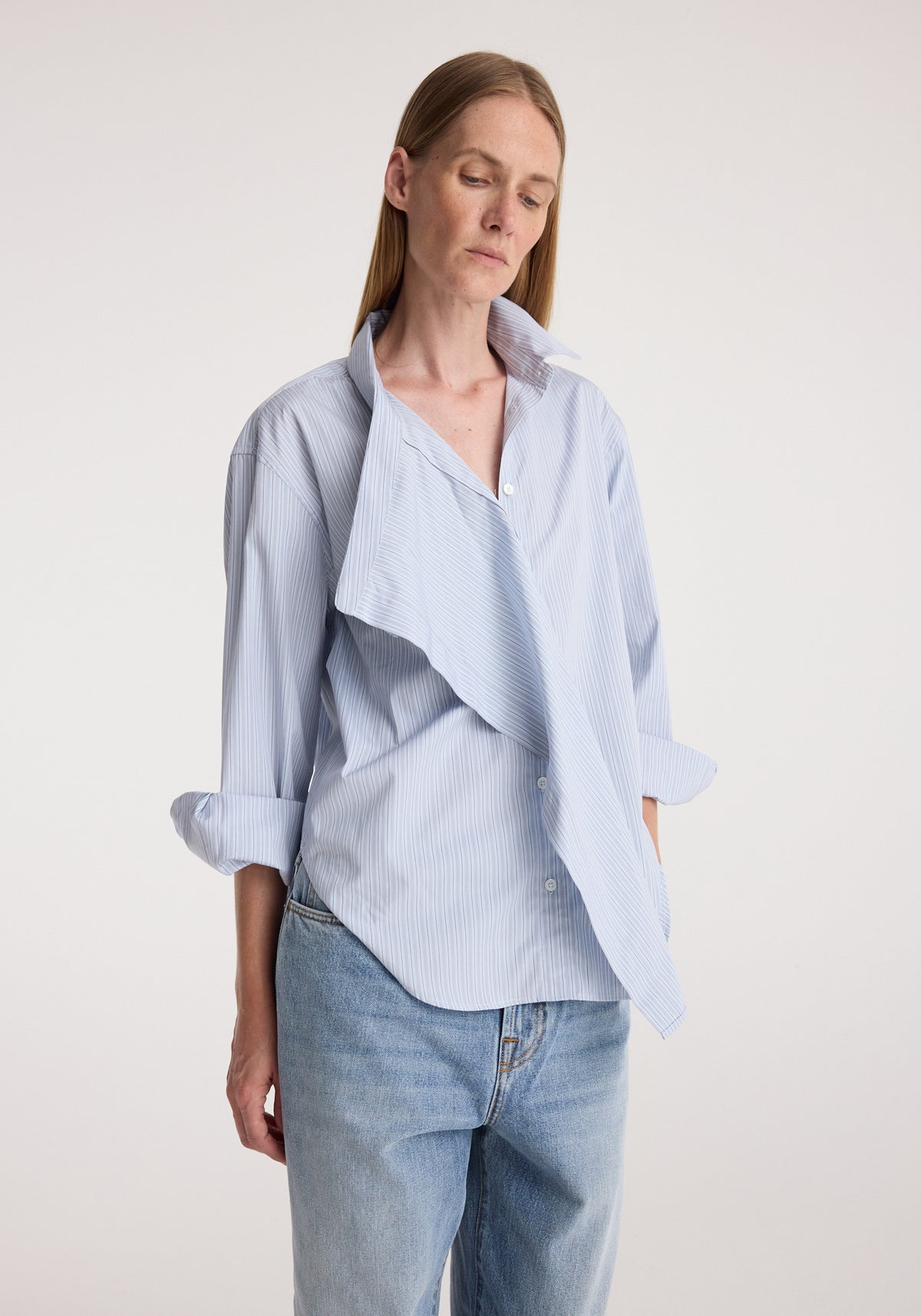 Draped collar shirt | blue stripe worn by a woman with rolled sleeves and light wash jeans against a neutral background