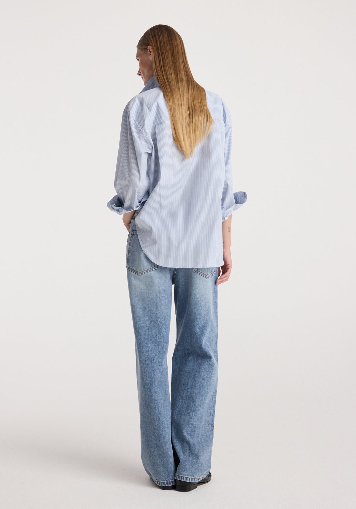 Draped collar shirt | blue stripe shown from the back on a model, featuring light blue stripes, rolled sleeves, a relaxed fit, and a curved hem