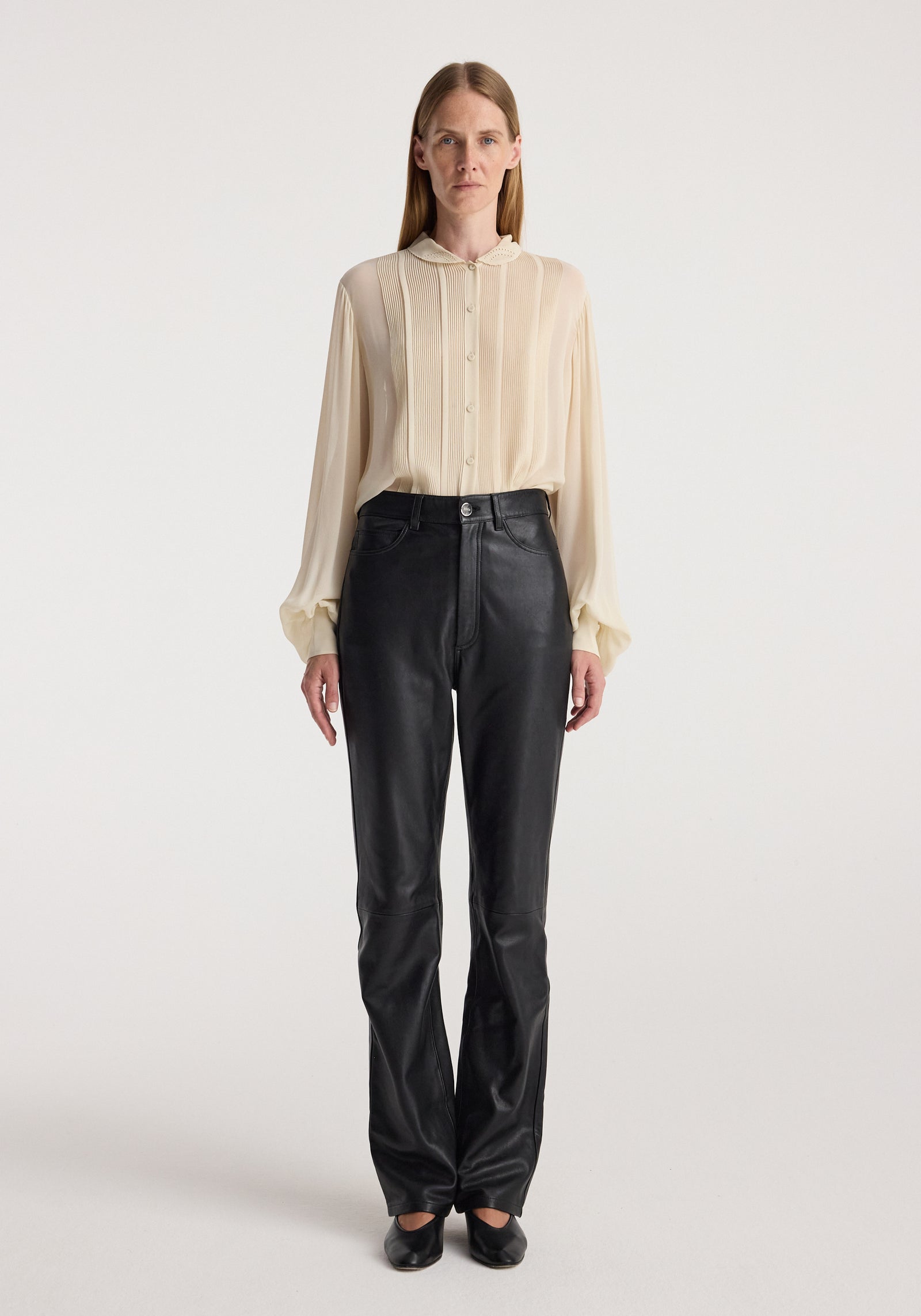 Woman wearing a cream long-sleeve button-up blouse with pleated detailing and gathered cuffs paired with black leather pants and black shoes, featuring Romantic top | cream.