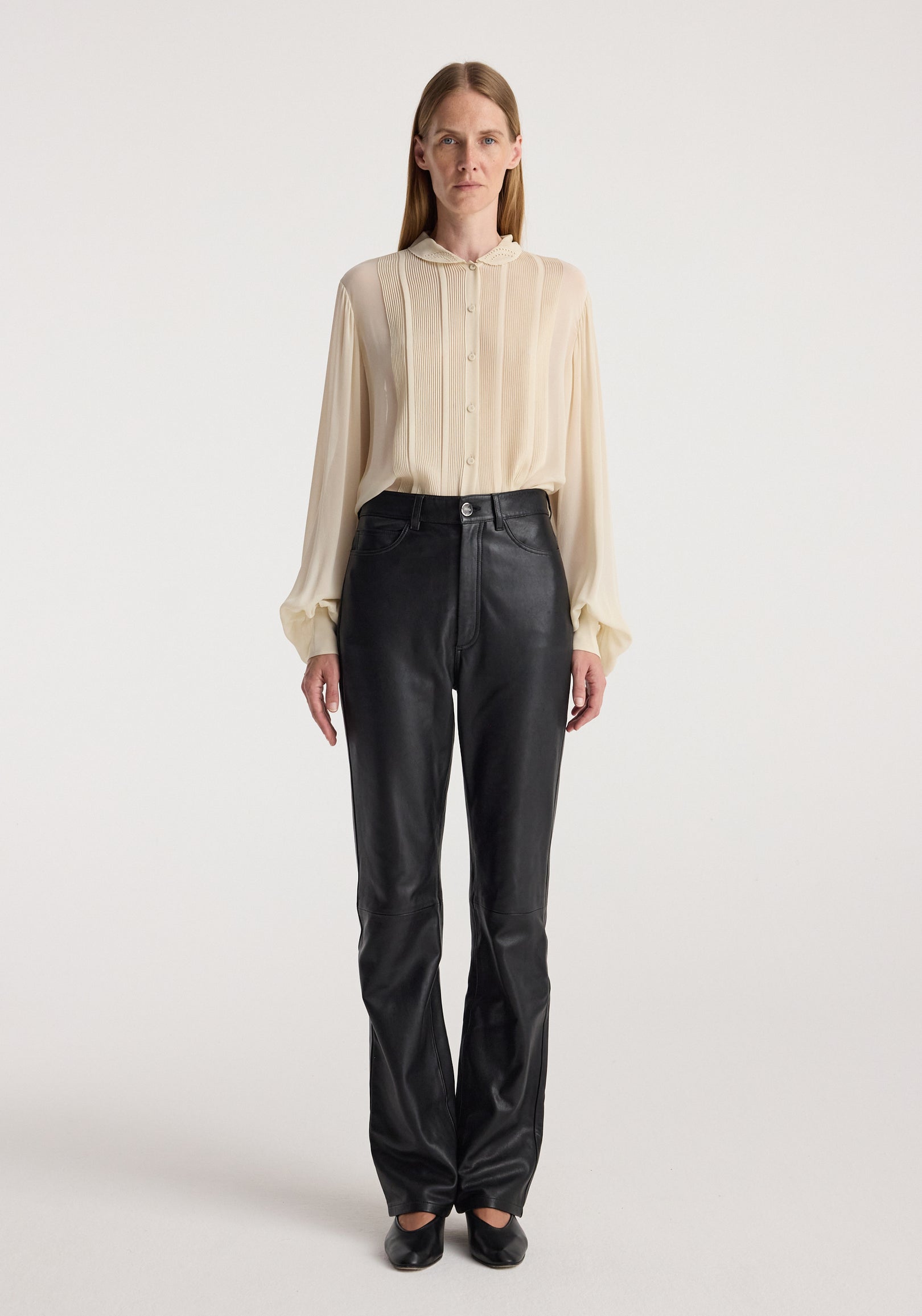 Woman wearing a cream long-sleeve button-up blouse with pleated detailing and gathered cuffs paired with black leather pants and black shoes, featuring Romantic top | cream.